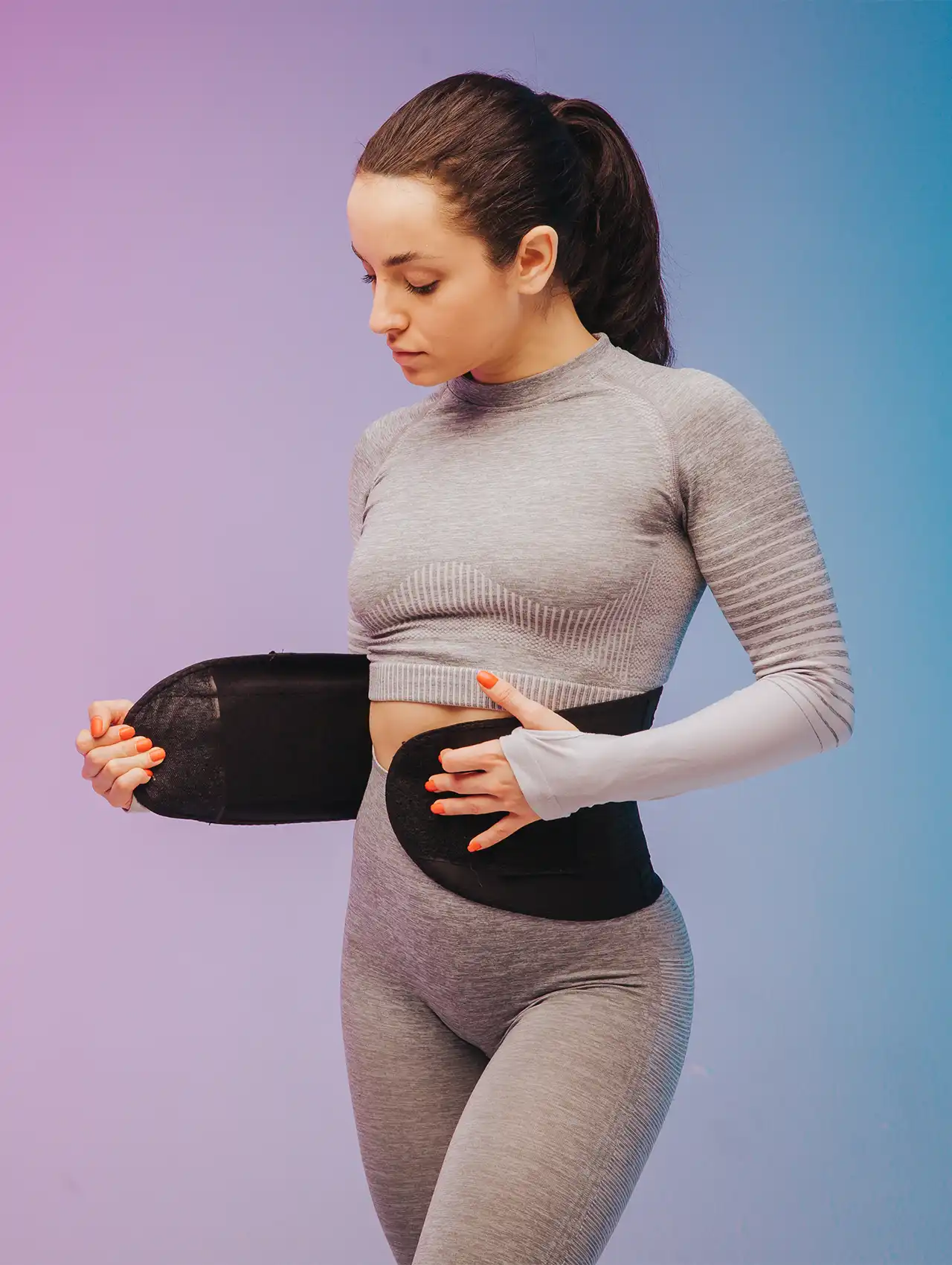 Woman in grey workout outfit adjusting a black waist trainer, highlighting fitness fashion and the question: do waist trainers work.