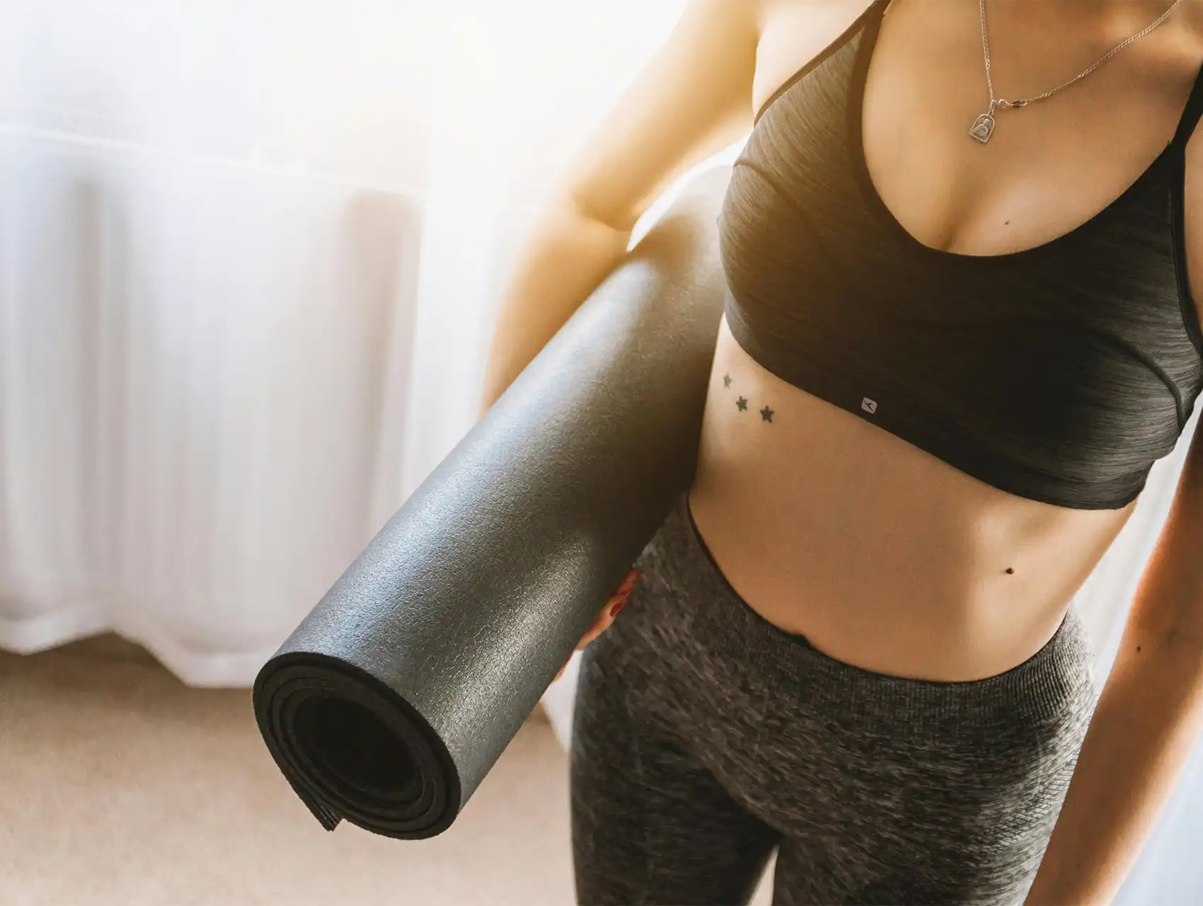Fit woman holding a yoga mat while wearing workout clothes, illustrating healthy lifestyle and the question: do waist trainers work.