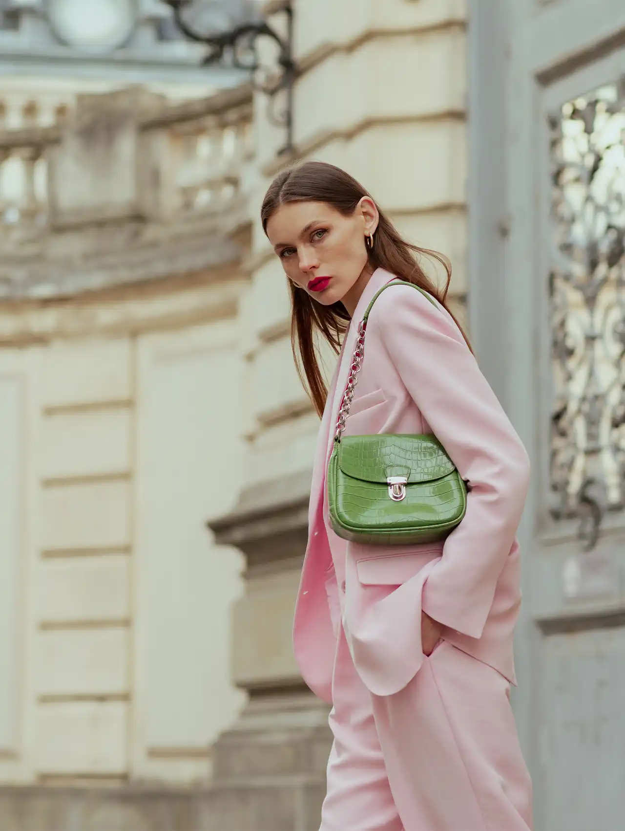 Woman in a light pink blazer for women styled with matching trousers and a green handbag.