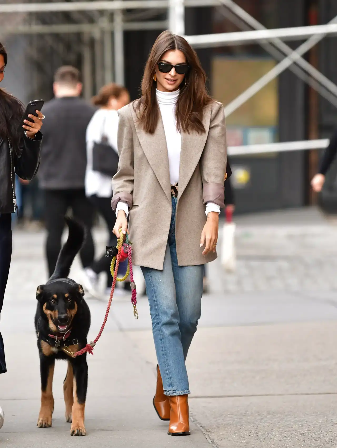 Emily Ratajkowski in a beige blazer, white turtleneck, and jeans while walking her dog, showcasing chic celebrity outfits.
