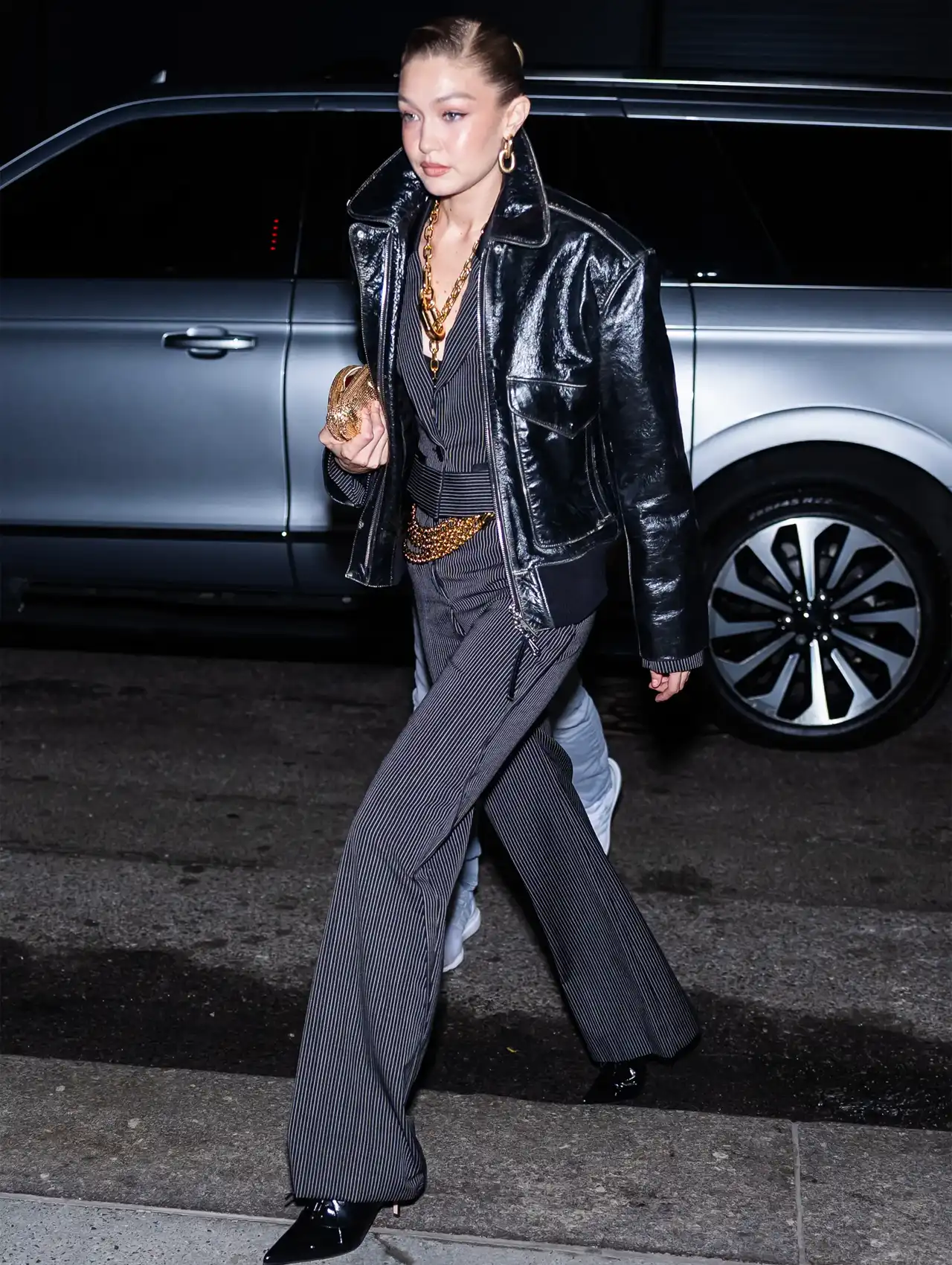 Gigi Hadid in a black leather jacket, pinstripe pants, and layered jewelry, a chic evening celebrity outfit.
