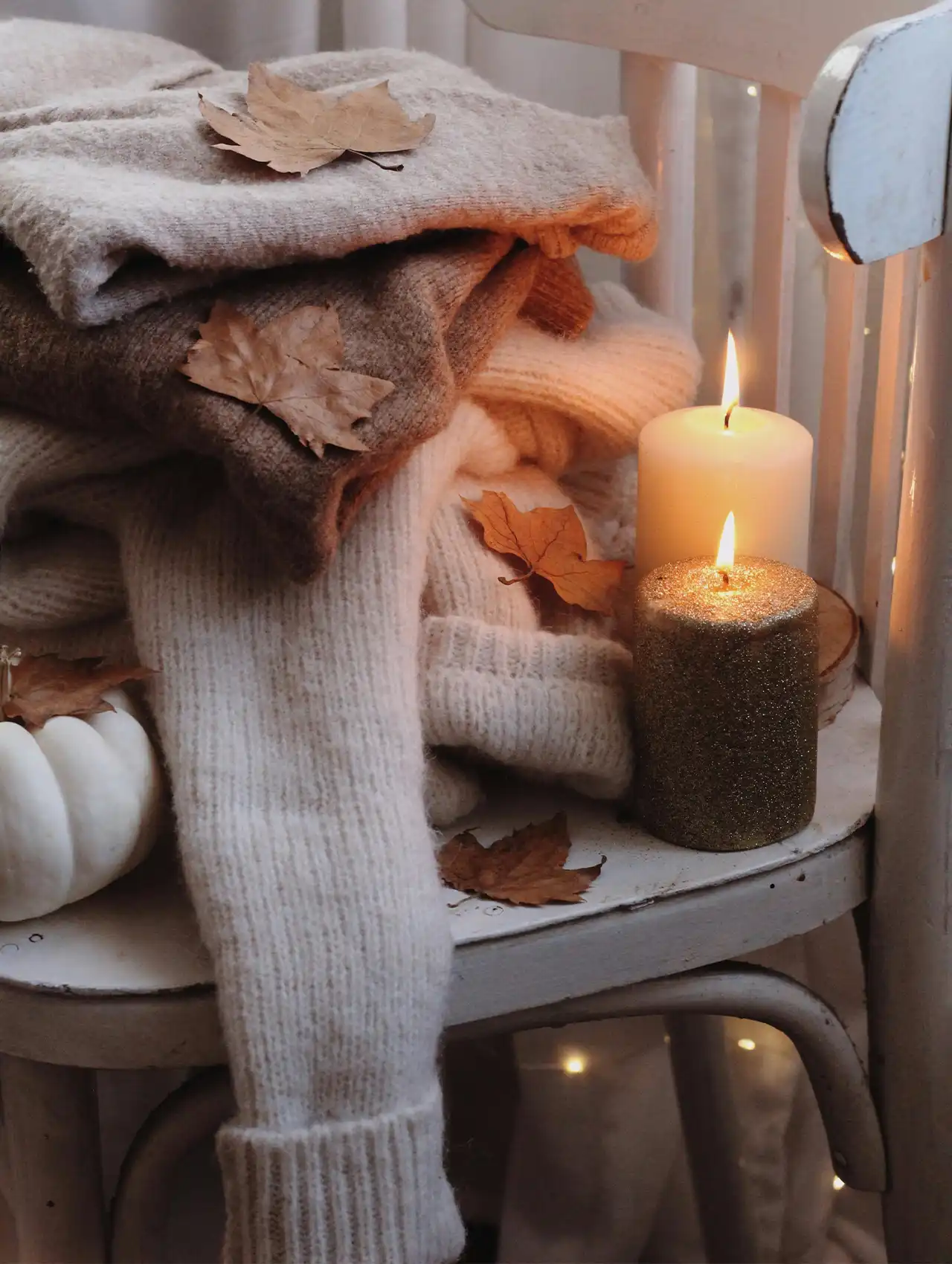 Cozy folded knit sweaters with candles and autumn leaves, perfect fall tops styling inspiration.