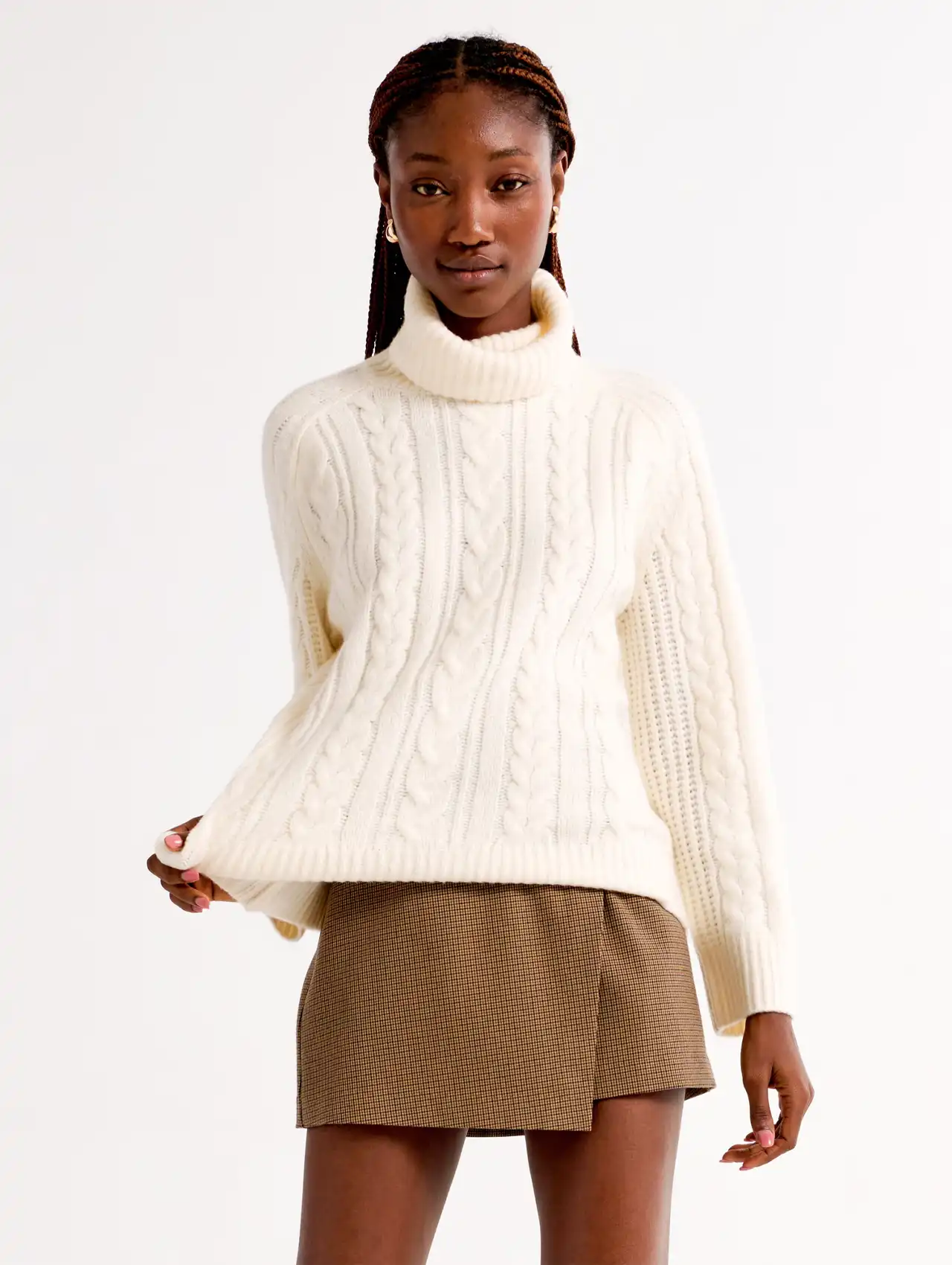 Cream cable-knit high-neck sweater paired with mini skirt, cozy fall tops fashion.