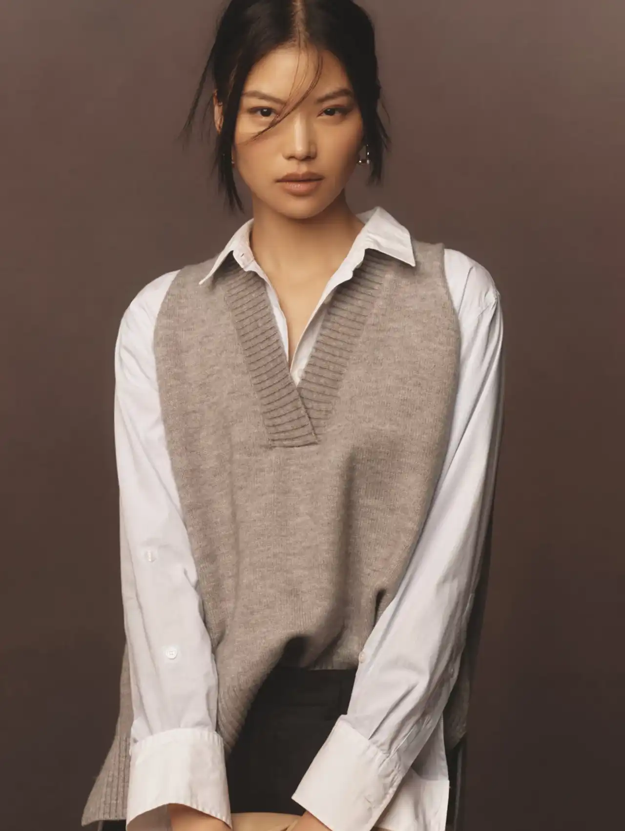 Oversized gray knit vest layered over white shirt, modern fall tops styling.