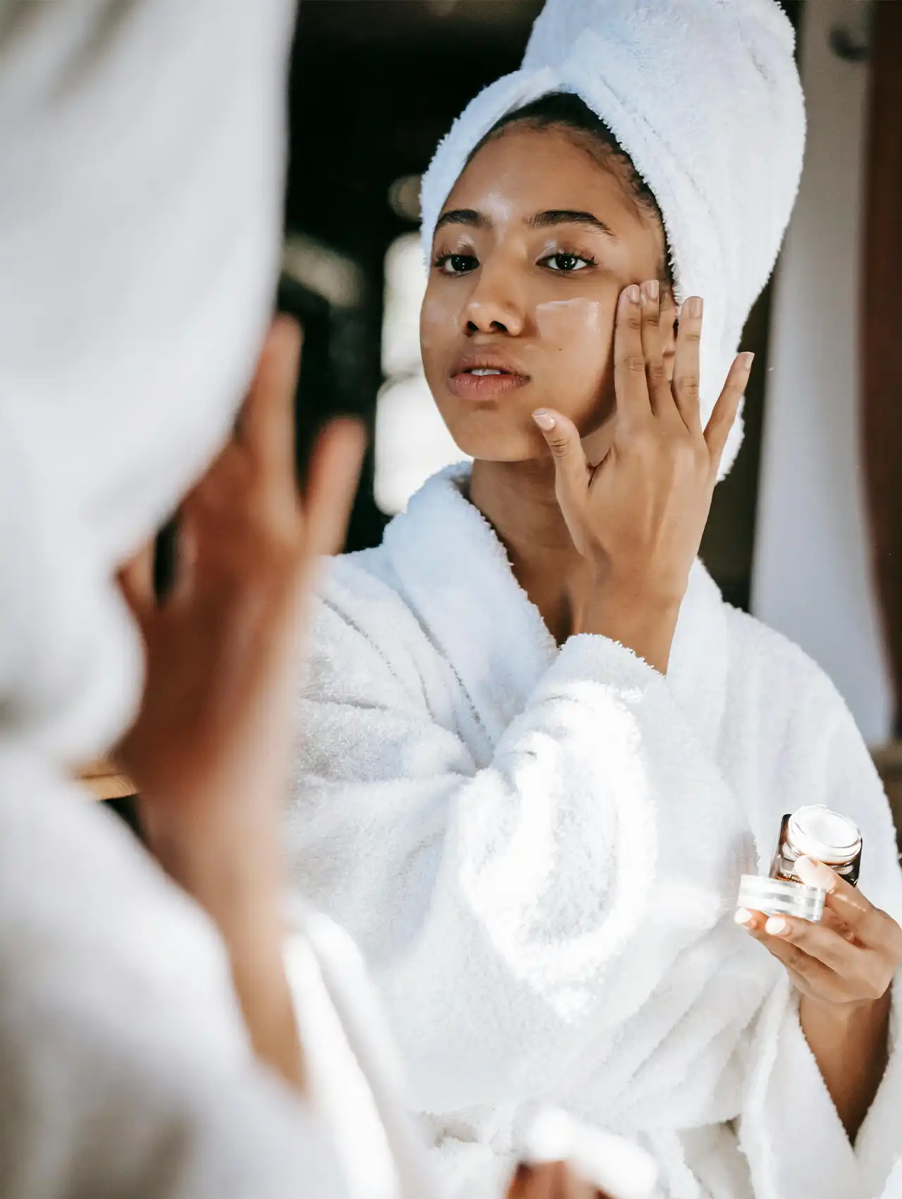 Woman applying cream to her face in front of a mirror as part of treatment for your acne routine