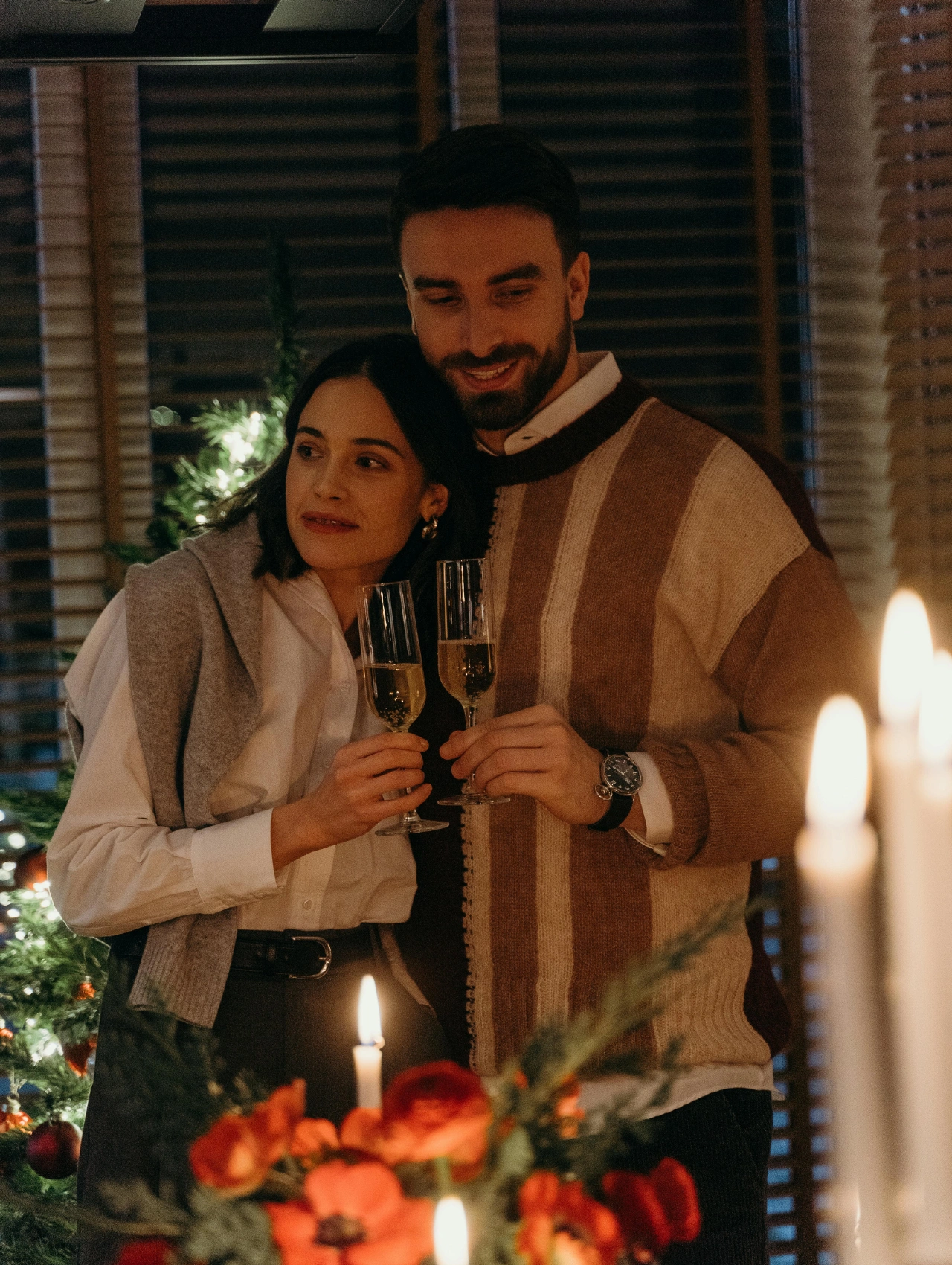 Couple enjoying a cozy evening toast during their Christmas Dinner, holding champagne glasses near a decorated tree.