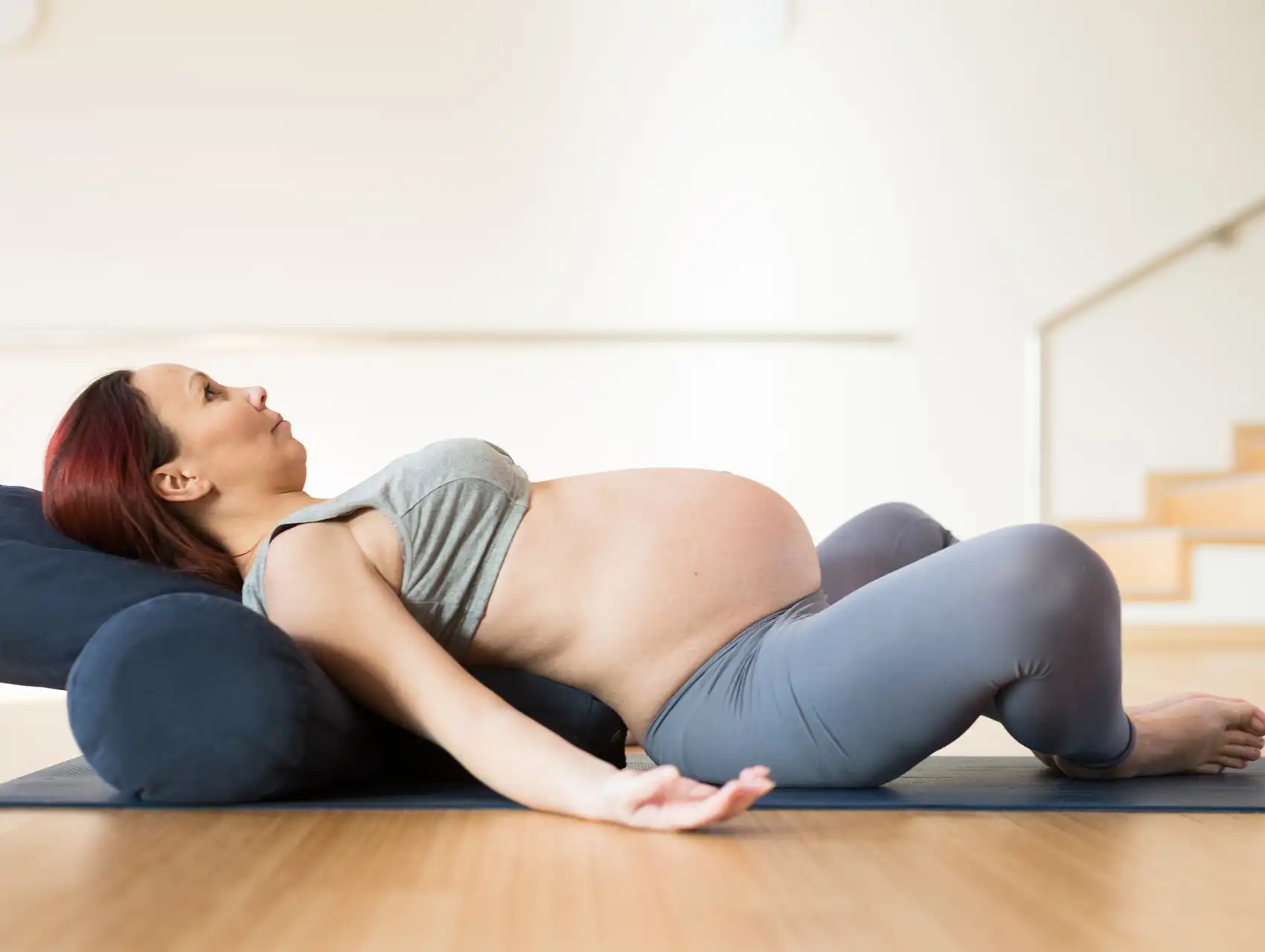 Pregnant woman reclining on blue bolster during prenatal yoga with bolsters