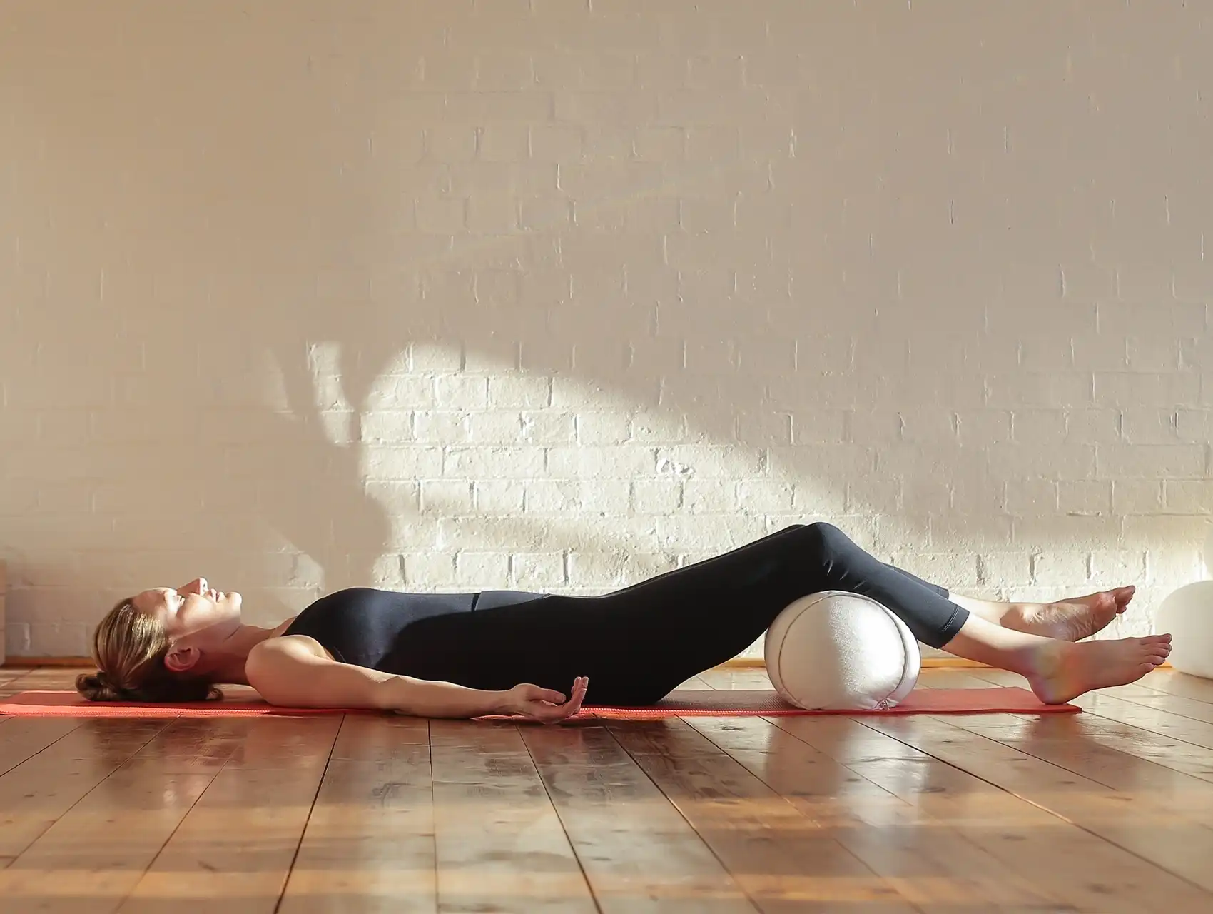 Woman lying in savasana with legs resting on white bolster with bolsters