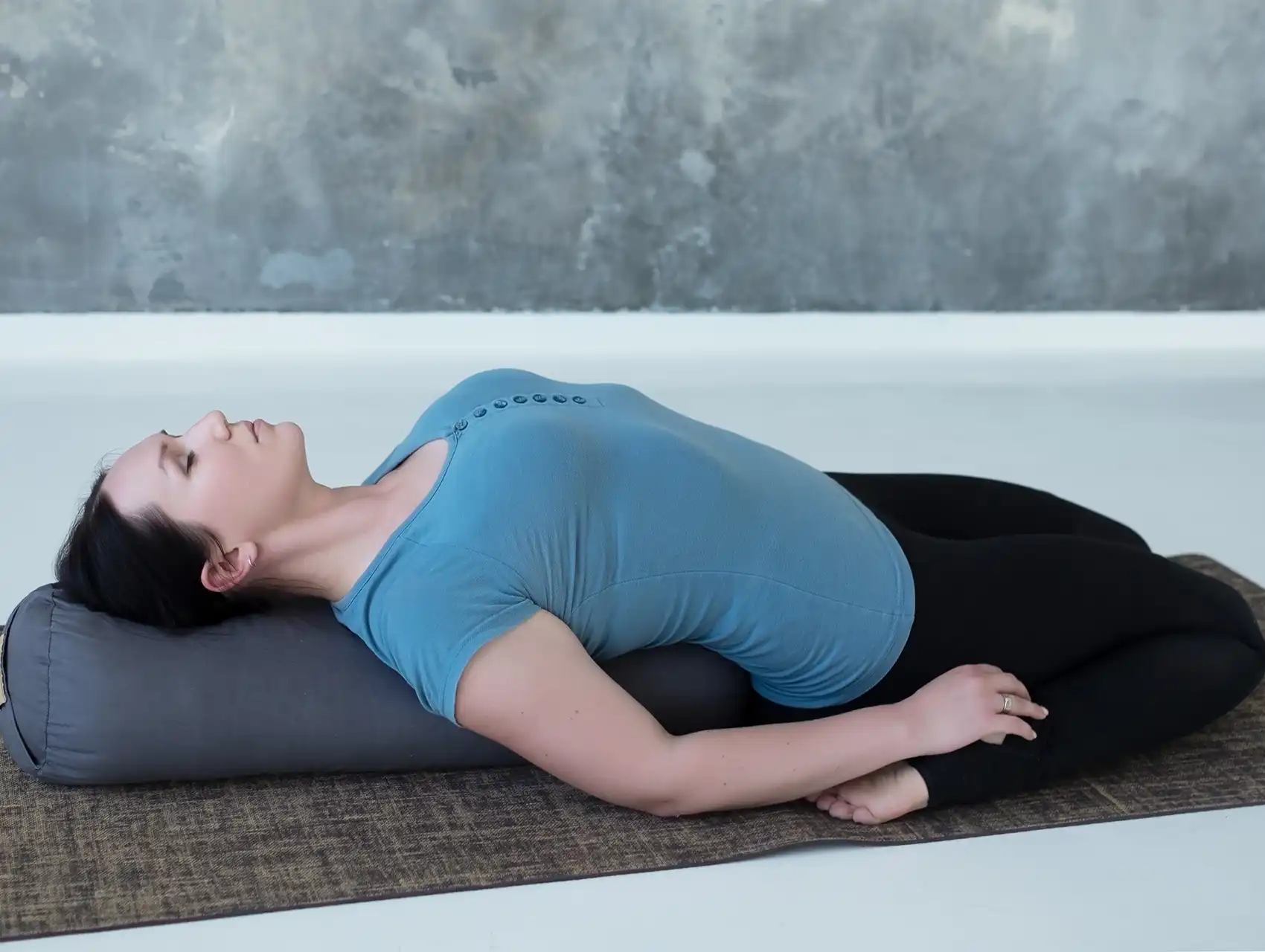 Woman practicing gentle backbend on gray yoga bolster for support with bolsters