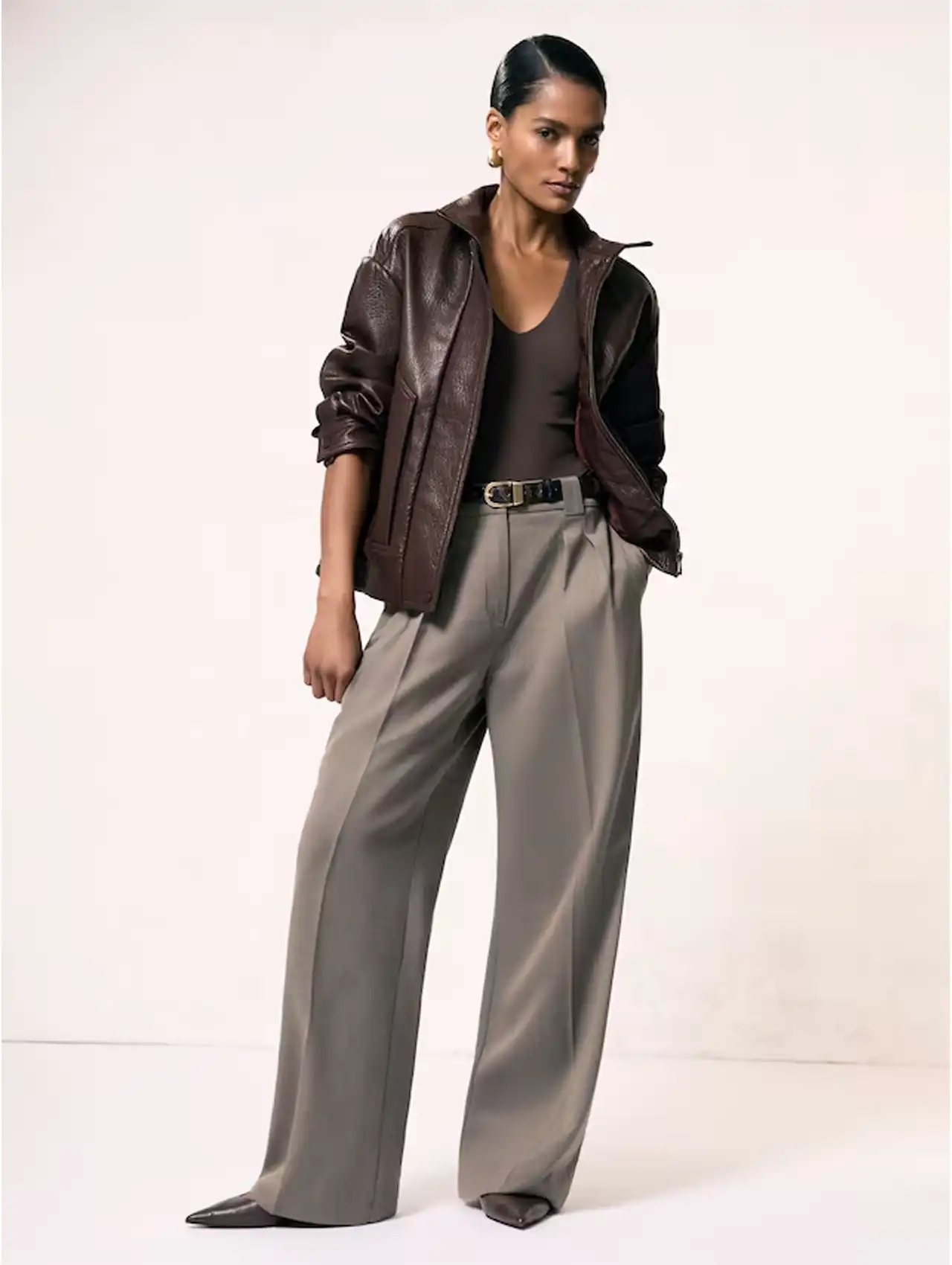 Stylish woman in brown bomber jacket with tailored high-waist trousers and a sleek top.