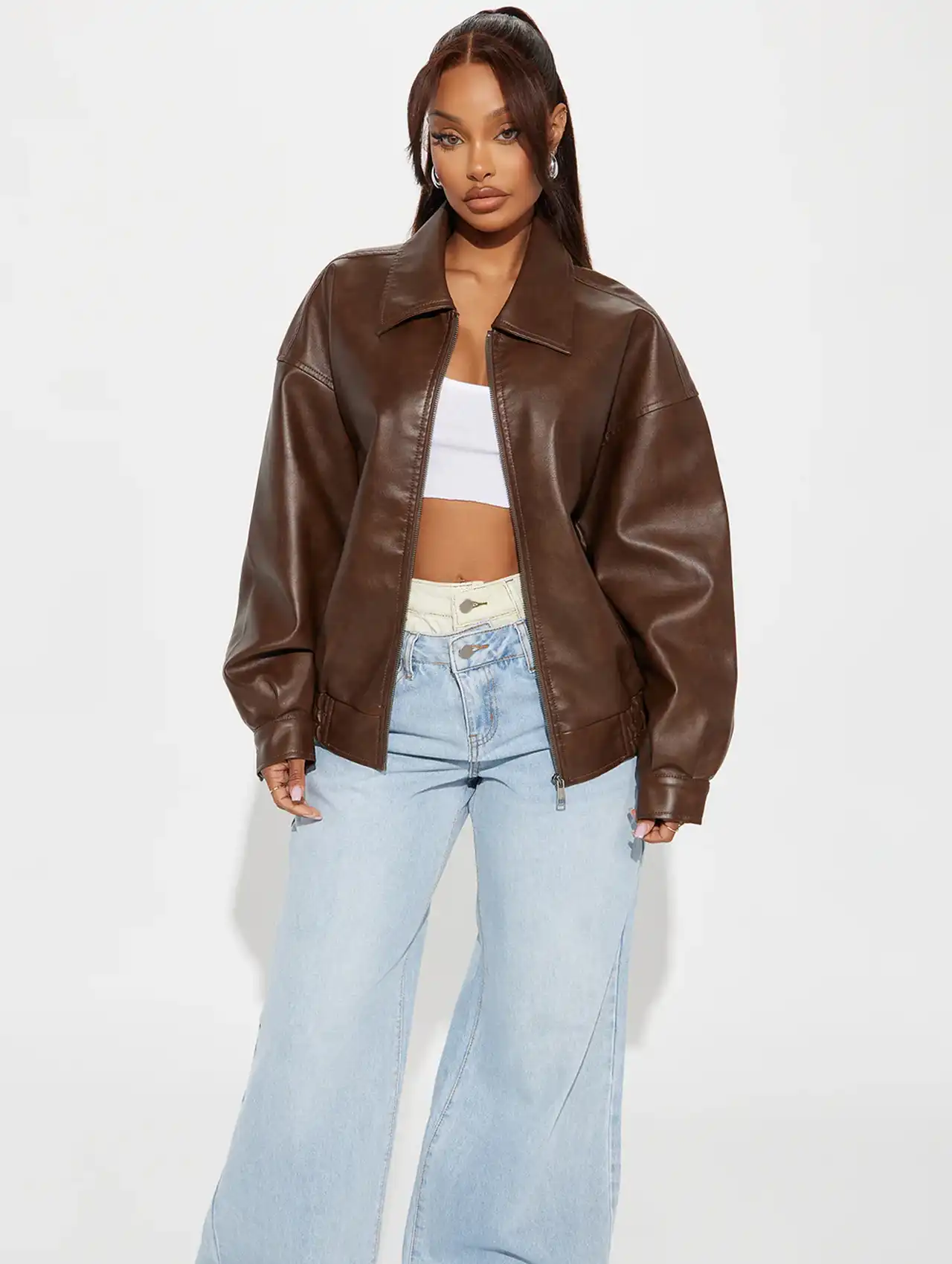 Model in brown bomber jacket styled with wide-leg jeans and a white crop top.