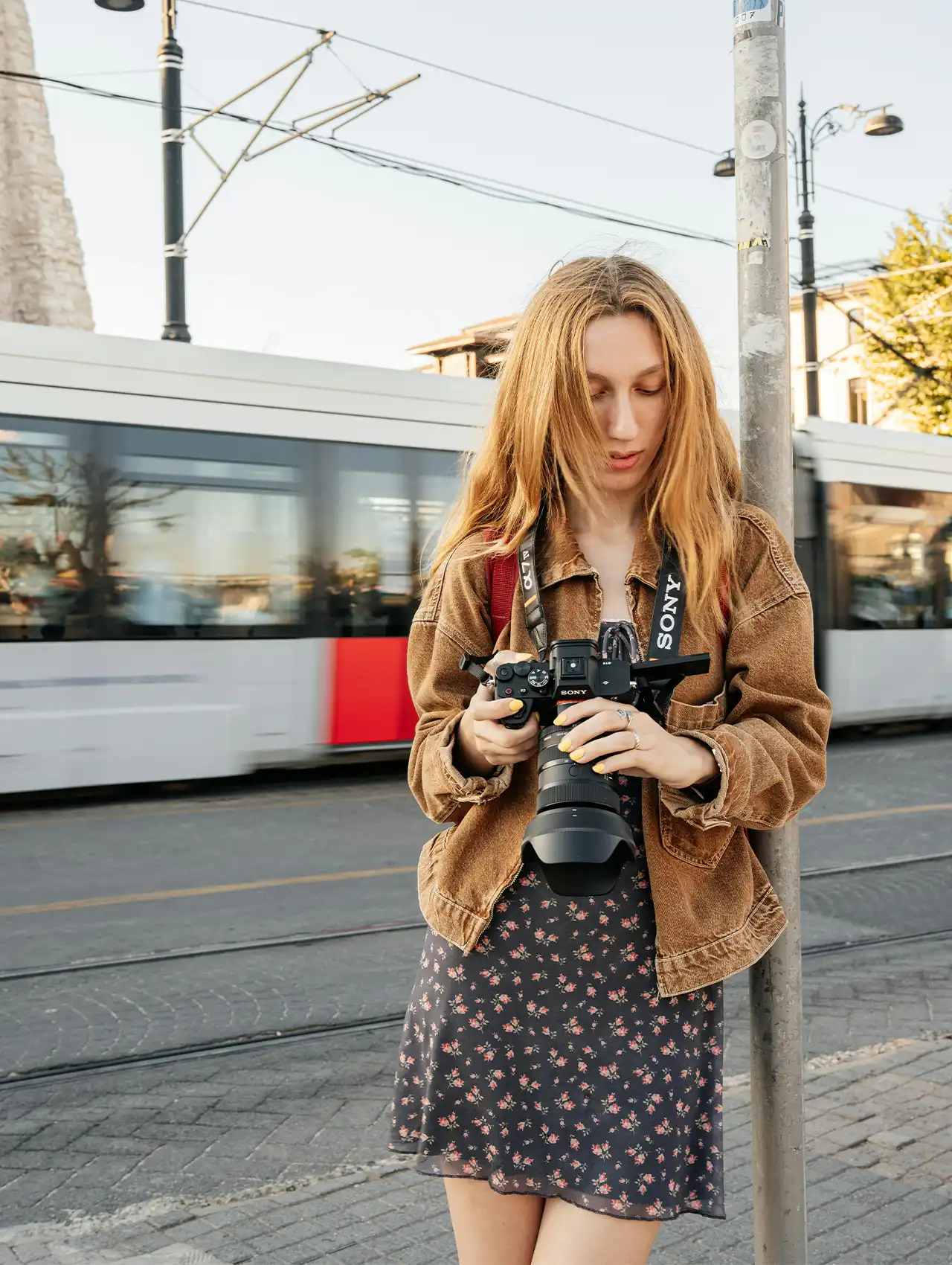Woman wearing a brown bomber jacket and holding a Sony camera on a city street, showcasing stylish brown bomber jackets.