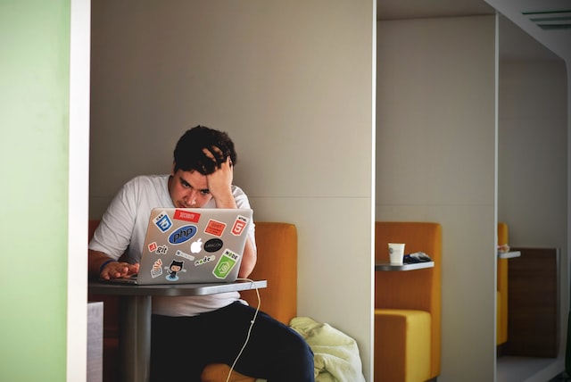 a young man in a white shirt sitting in a booth with a laptop depicting the college student stress management guide 