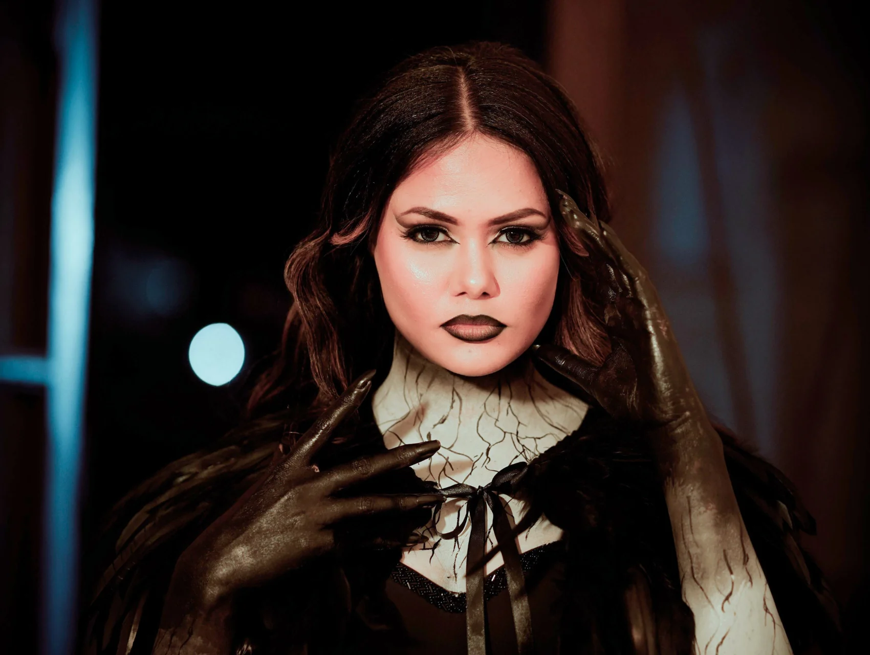 Dark Halloween makeup look with winged liner, brown matte lips, cracked vein detail on the neck, and black painted hands