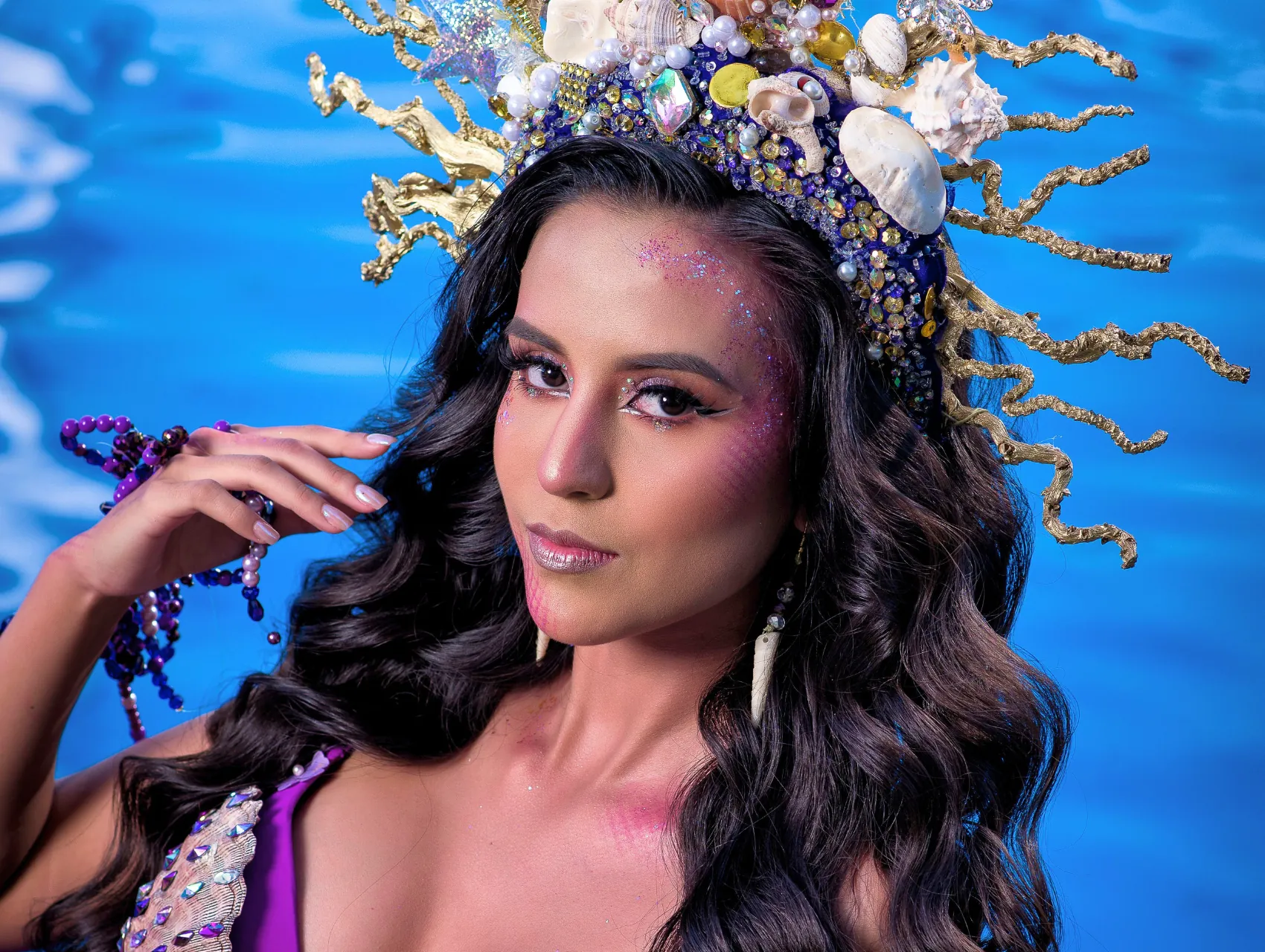 Mermaid Halloween makeup look with pink glitter, netted scale texture on the cheek, metallic lips, and a seashell crown
