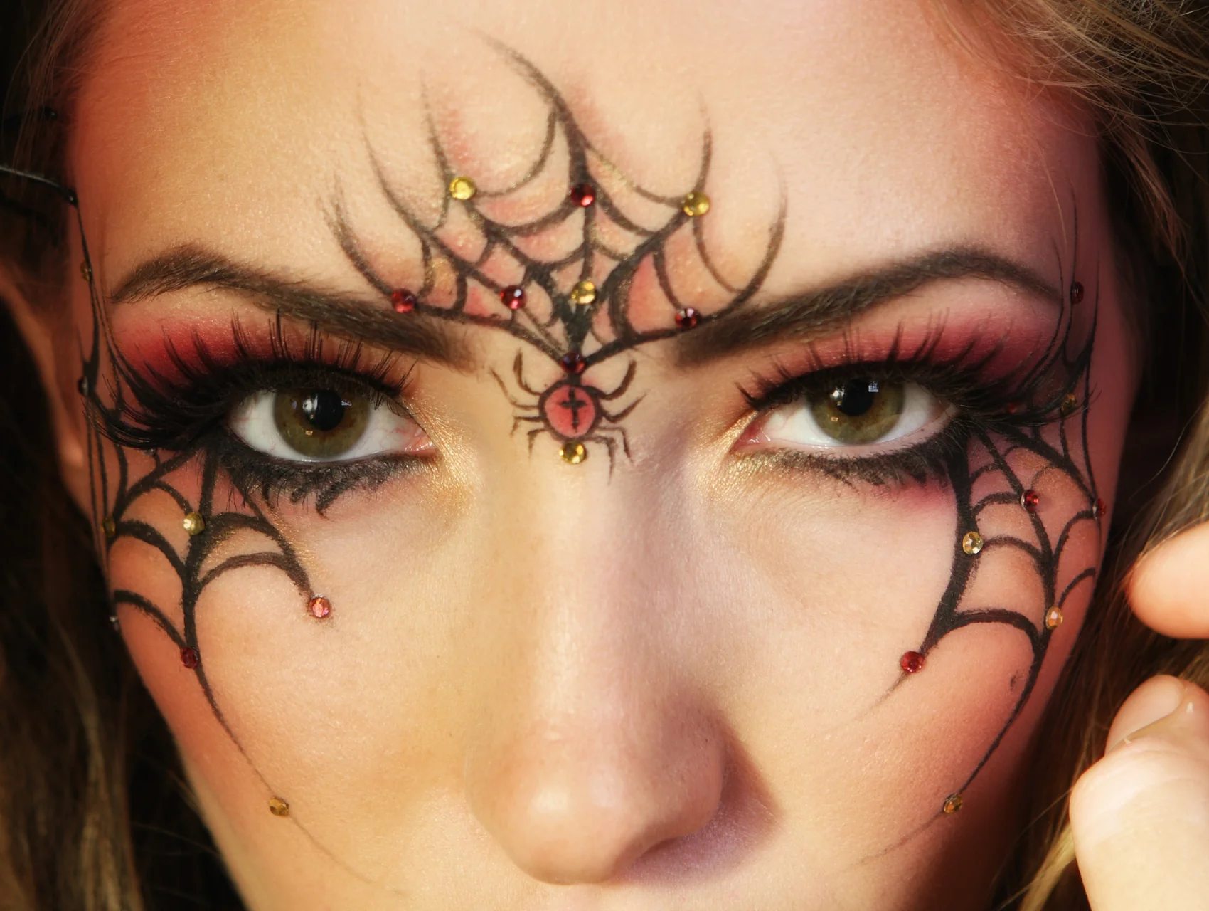 Spider web eyeliner Halloween makeup look in black liquid liner with red and gold rhinestones and a spider between the brows