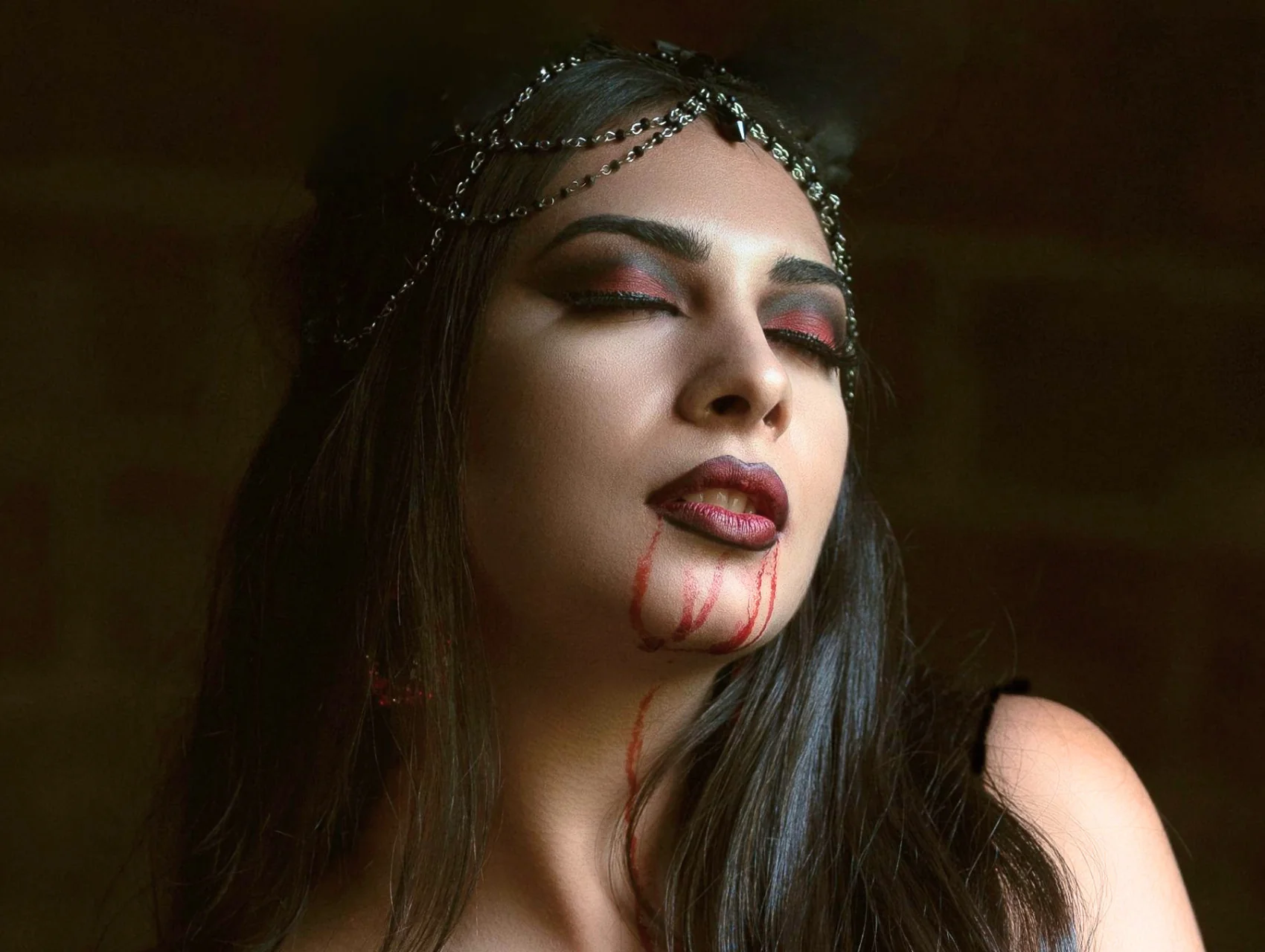 Vampire Halloween makeup look with red and charcoal smoky eyes, ombre berry lips, and faux blood dripping from the mouth