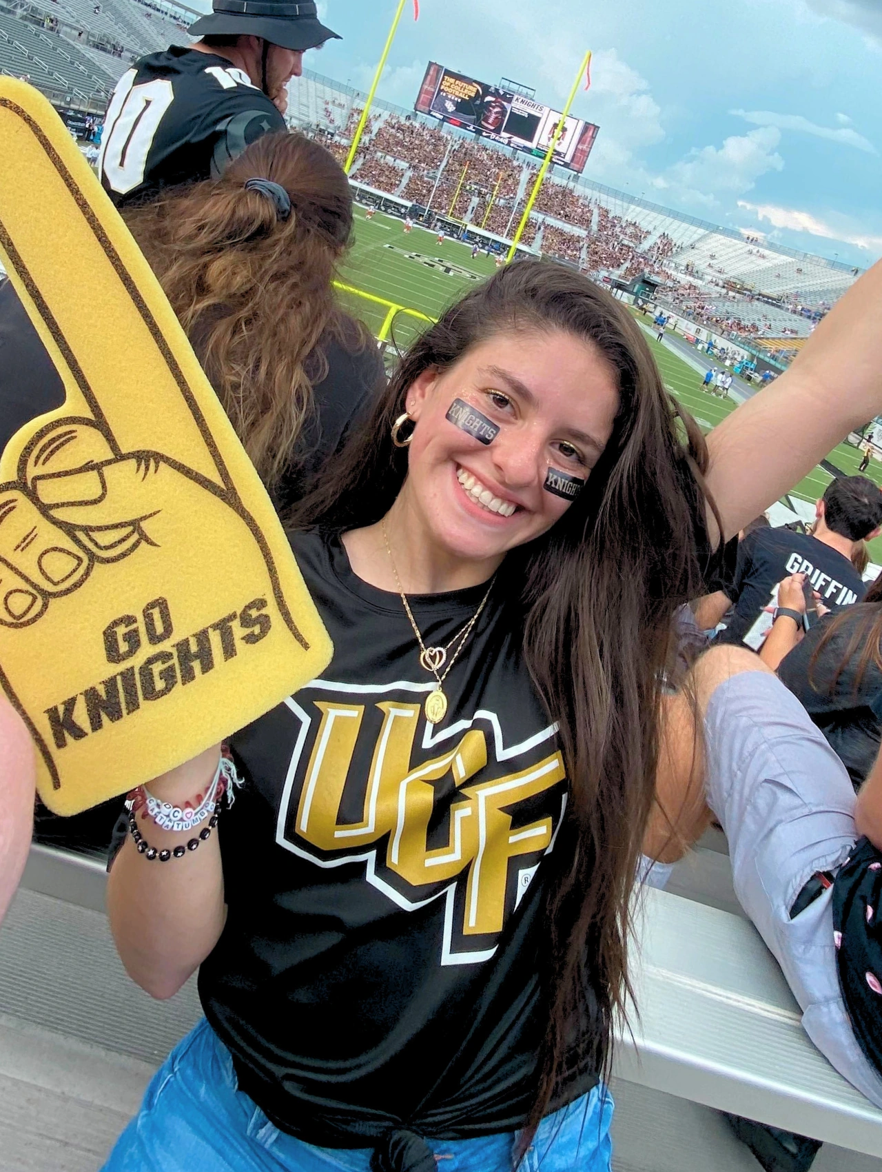 Woman in UCF gear smiling at a football game, showcasing trendy tailgate outfits for college game day.
