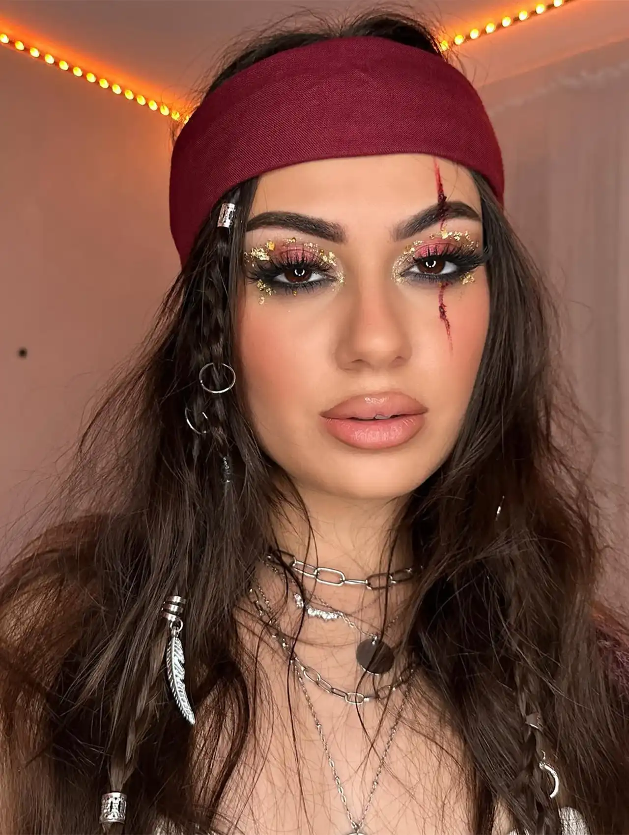 Pirate-themed halloween makeup looks with scar detail, red headband, and layered necklaces.
