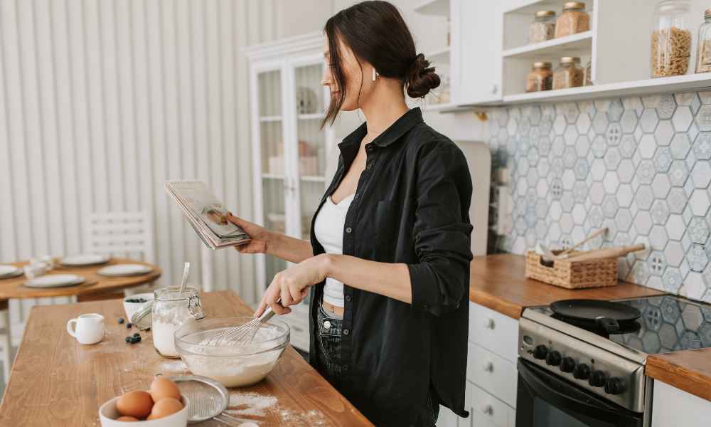 Woman with cooking book following recipe that she is making on the counter
