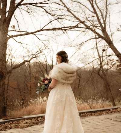 Woman in her bride dress and fur coat holding bouquet