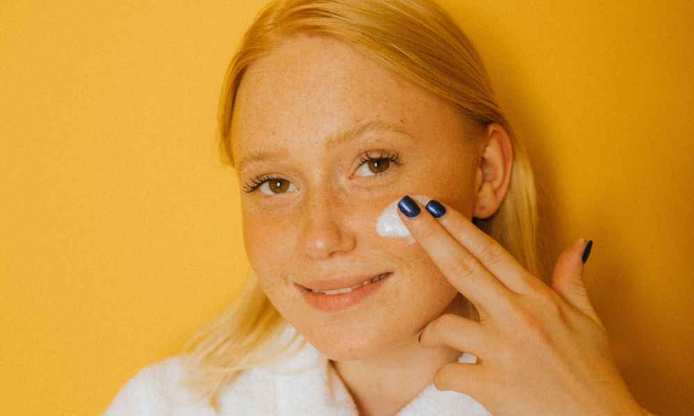 Woman smiling while putting on moisturizer 