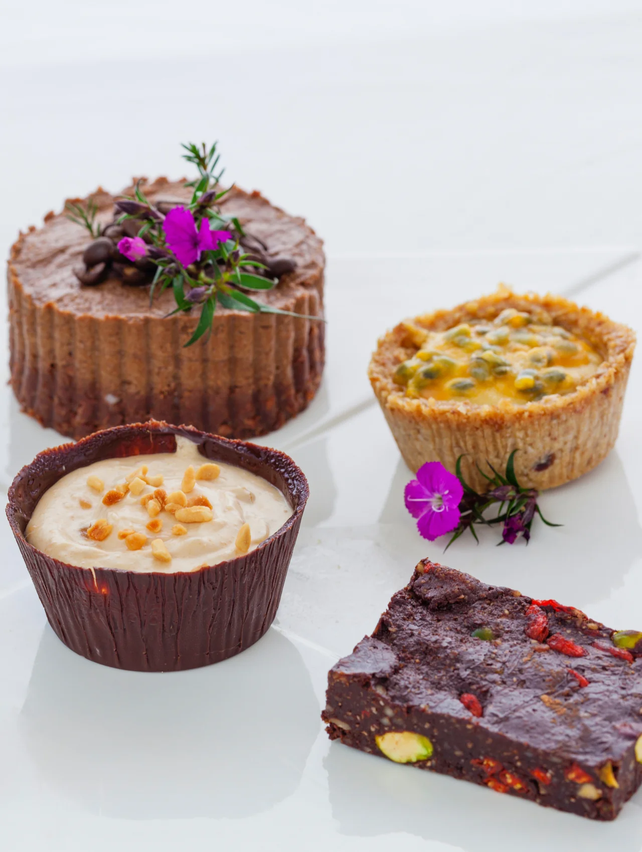 Vegan desserts including chocolate peanut butter cups, a passion fruit tart, a mousse cake, and a pistachio fudge bar