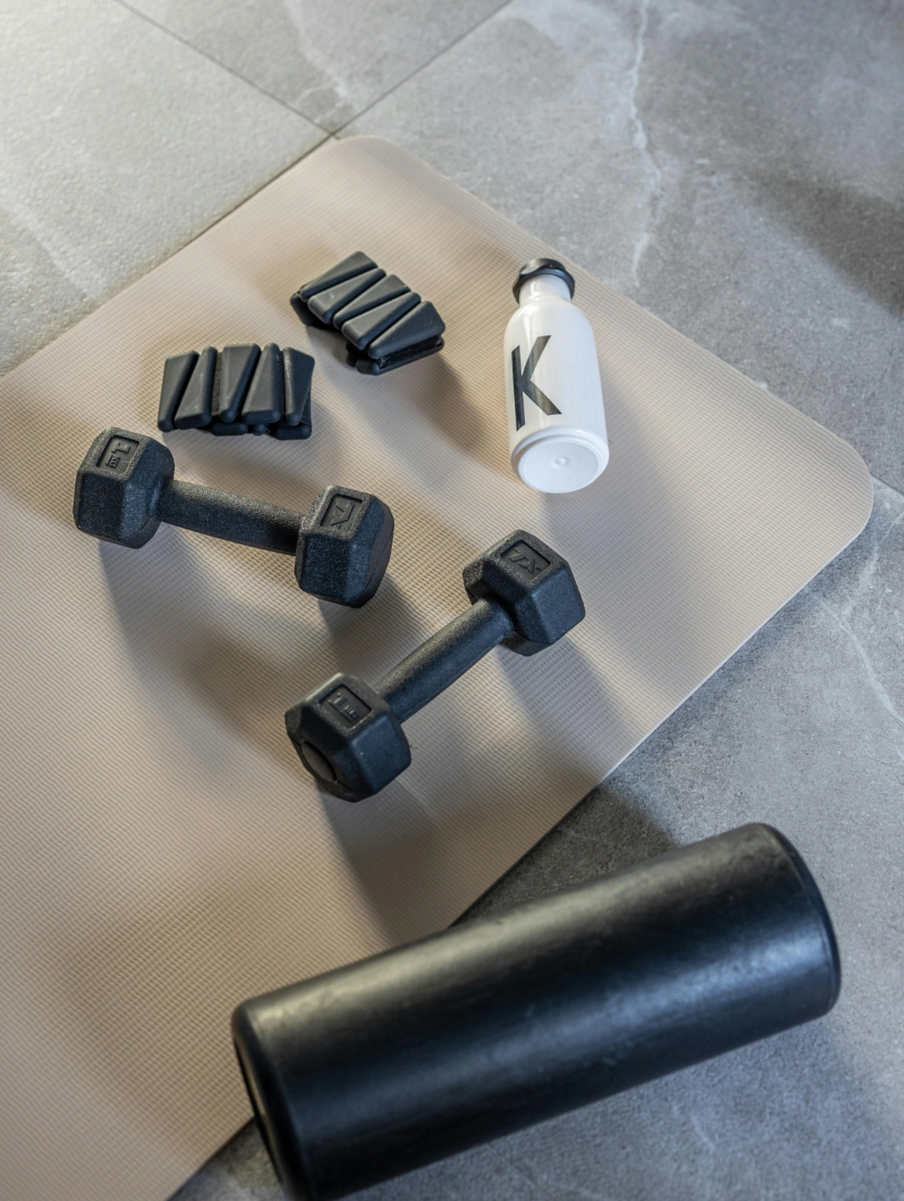 Your workout gear – gym essentials for beginners, dumbbells and a water bottle set on a mat with small fitness accessories.