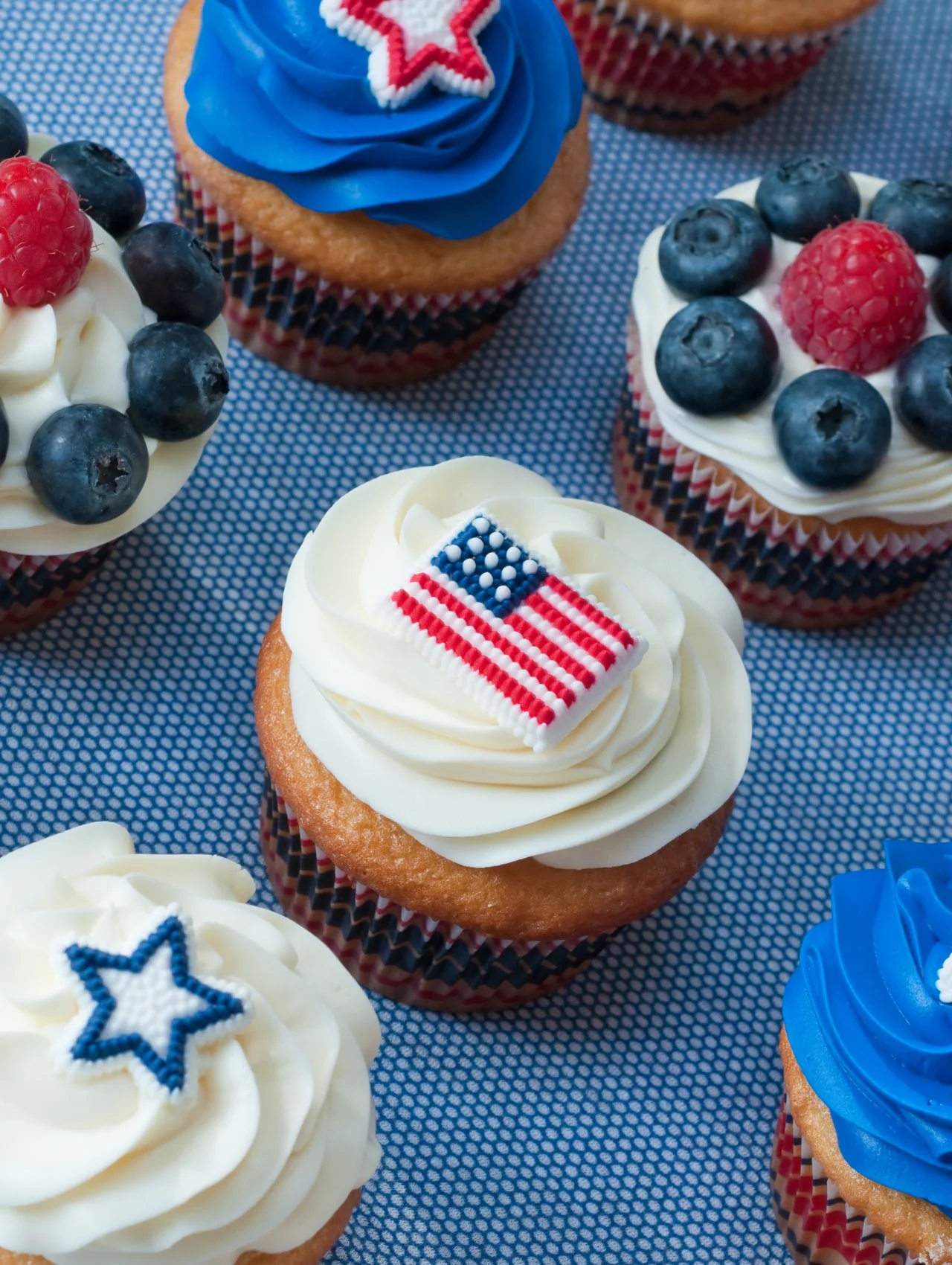 Patriotic 4th of July cupcakes with red, white, and blue frosting, berries, and American flag toppers for party ideas