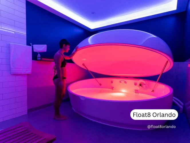 A woman in a dimly lit spa room preparing to enter a futuristic floatation therapy pod illuminated with pink and purple light.