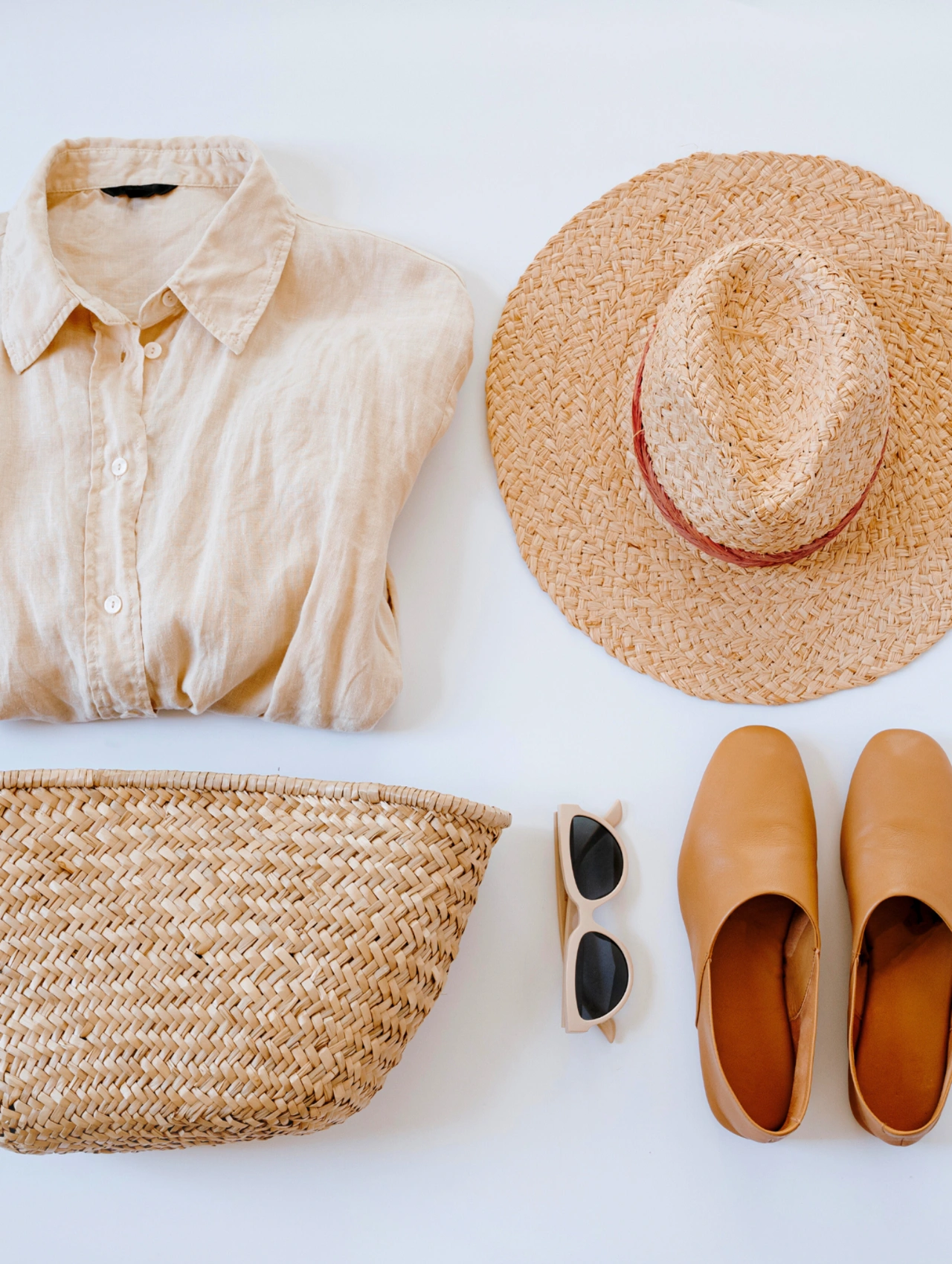 Para finalizar viaje a la playa: conjunto minimalista de accesorios veraniegos con camisa beige, sombrero de paja, bolso tejido, gafas de sol y zapatos planos ideales para un viaje a la playa.