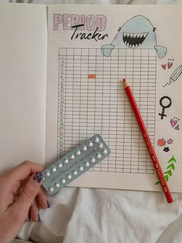 a hand holding a pill and a red pencil on a bullet journal