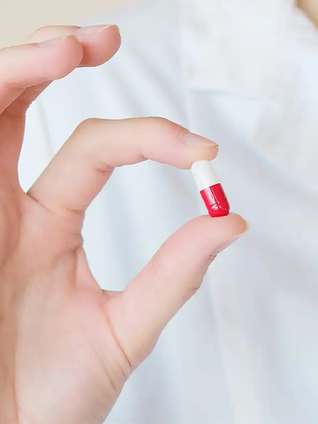 a hand holding a red and white pill