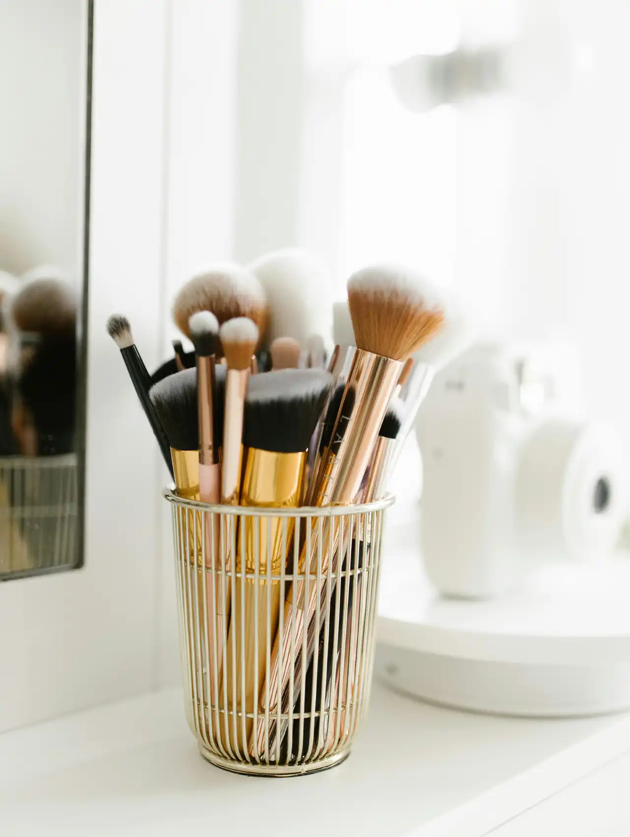 Vaso dorado con brochas de maquillaje sobre tocador de maquillaje moderno.