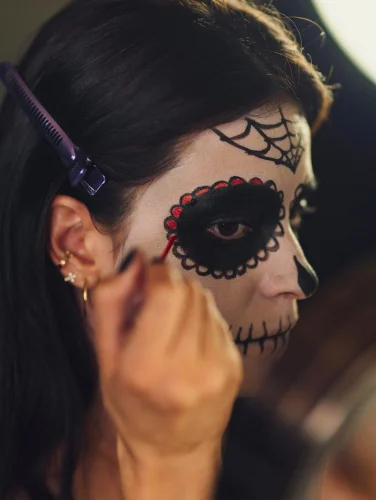Mujer aplicando maquillaje para Halloween con diseño de calavera en el rostro, mostrando un estilo creativo y detallado.