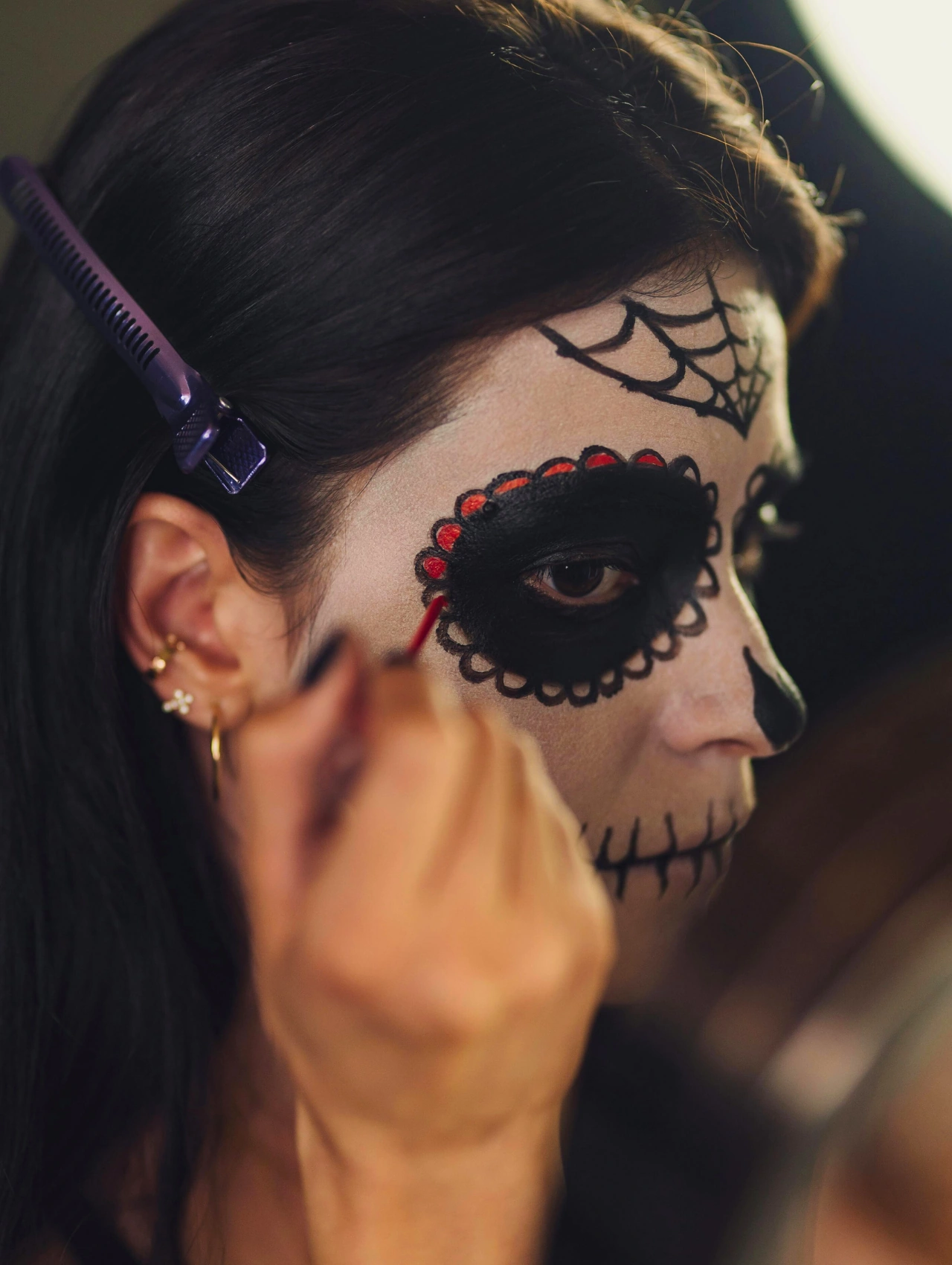 Mujer aplicando maquillaje para Halloween con diseño de calavera en el rostro, mostrando un estilo creativo y detallado.
