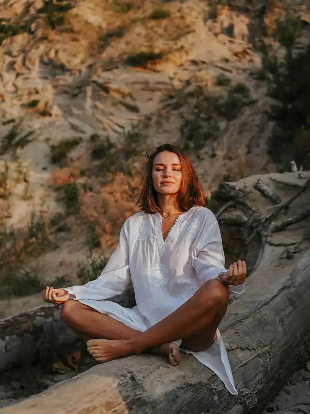 a woman sitting on a log with her eyes closed