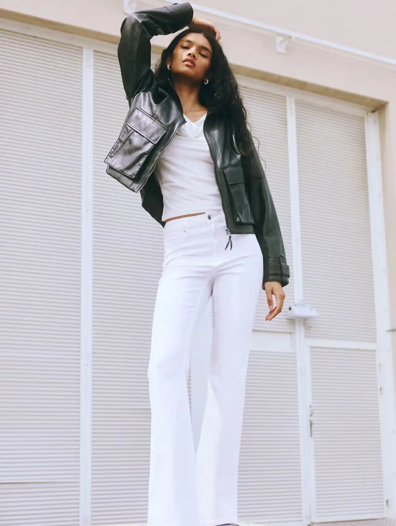 Woman wearing white high-waisted flare jeans with black leather jacket, fall clothing for women