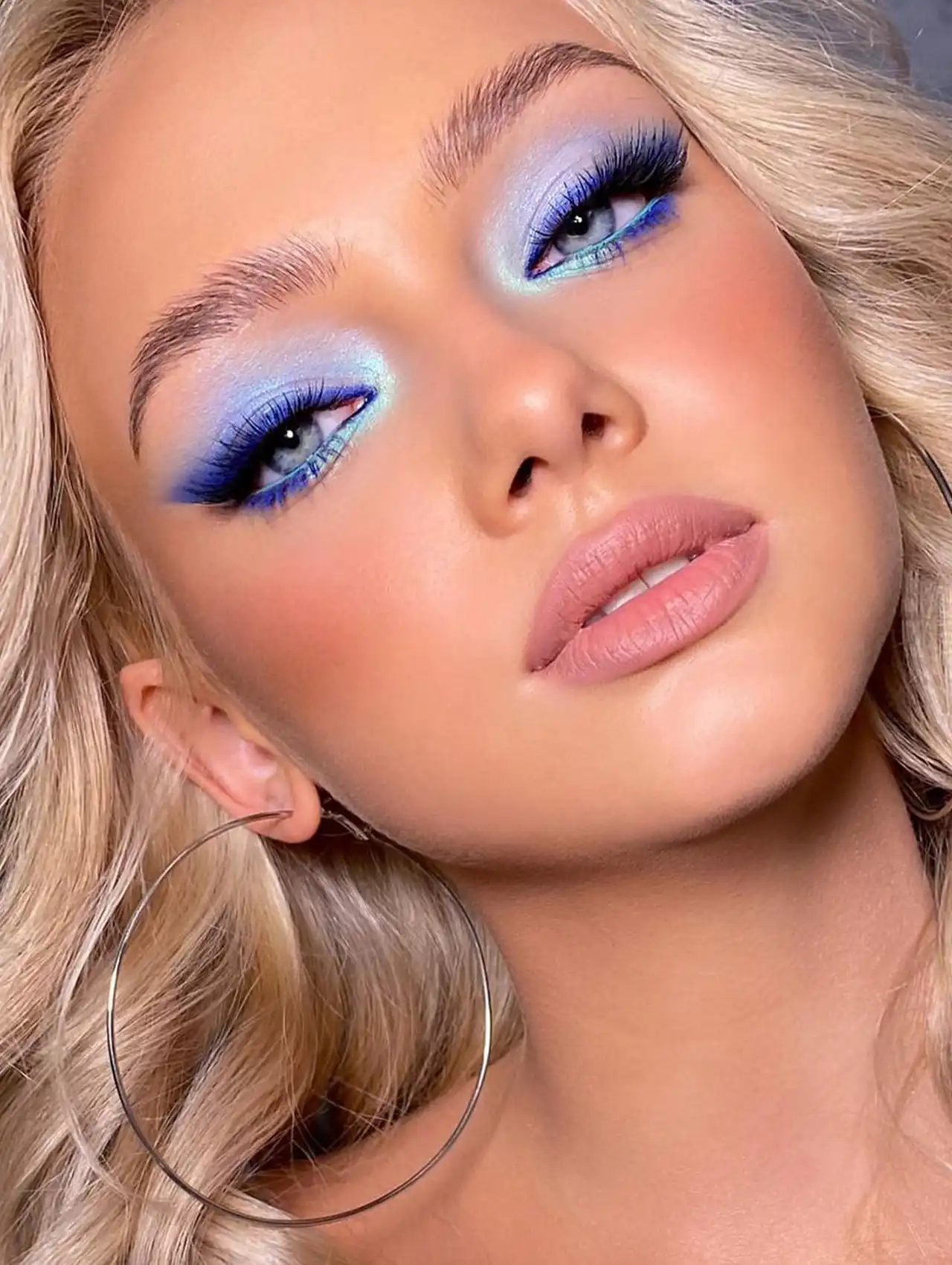 Mujer con maquillaje brillante y delineador de ojos azul combinado con sombras plateadas.