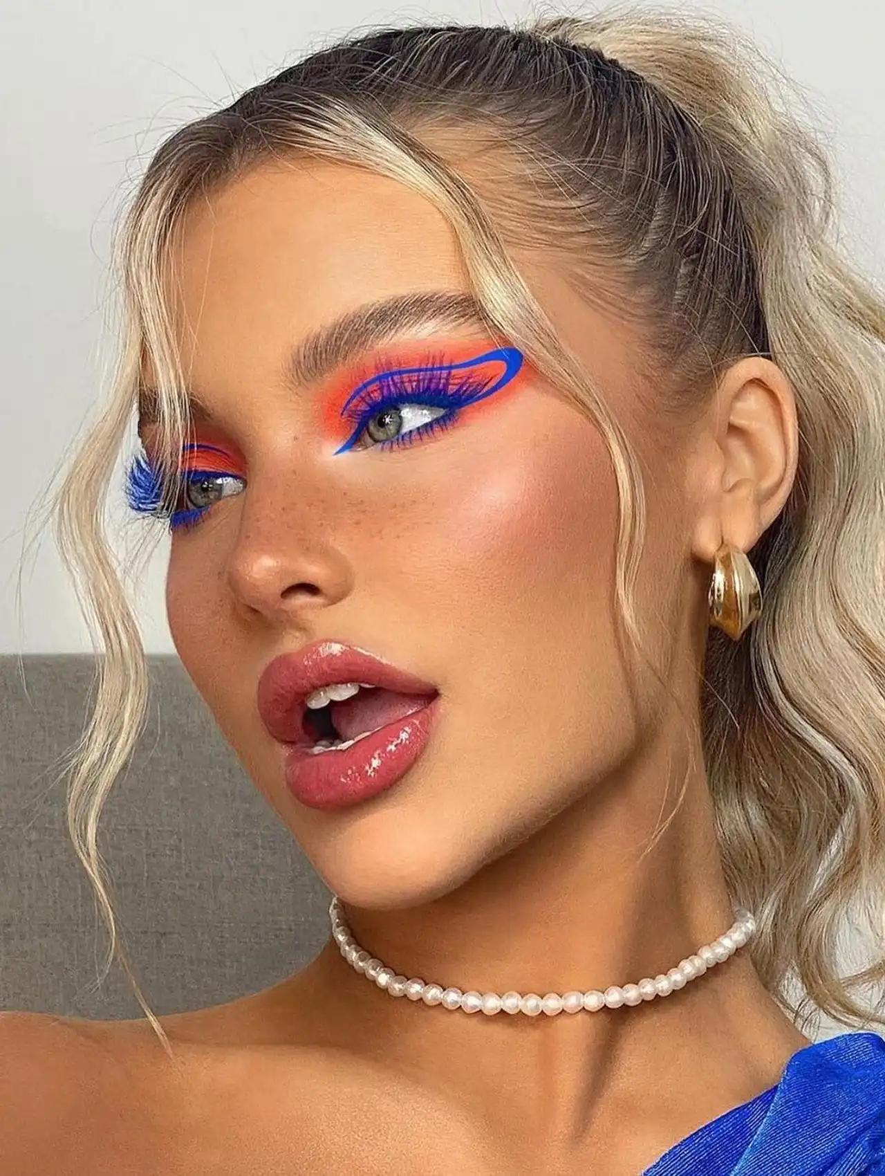 Mujer con maquillaje artístico y delineador de ojos azul en diseño gráfico ondulado.