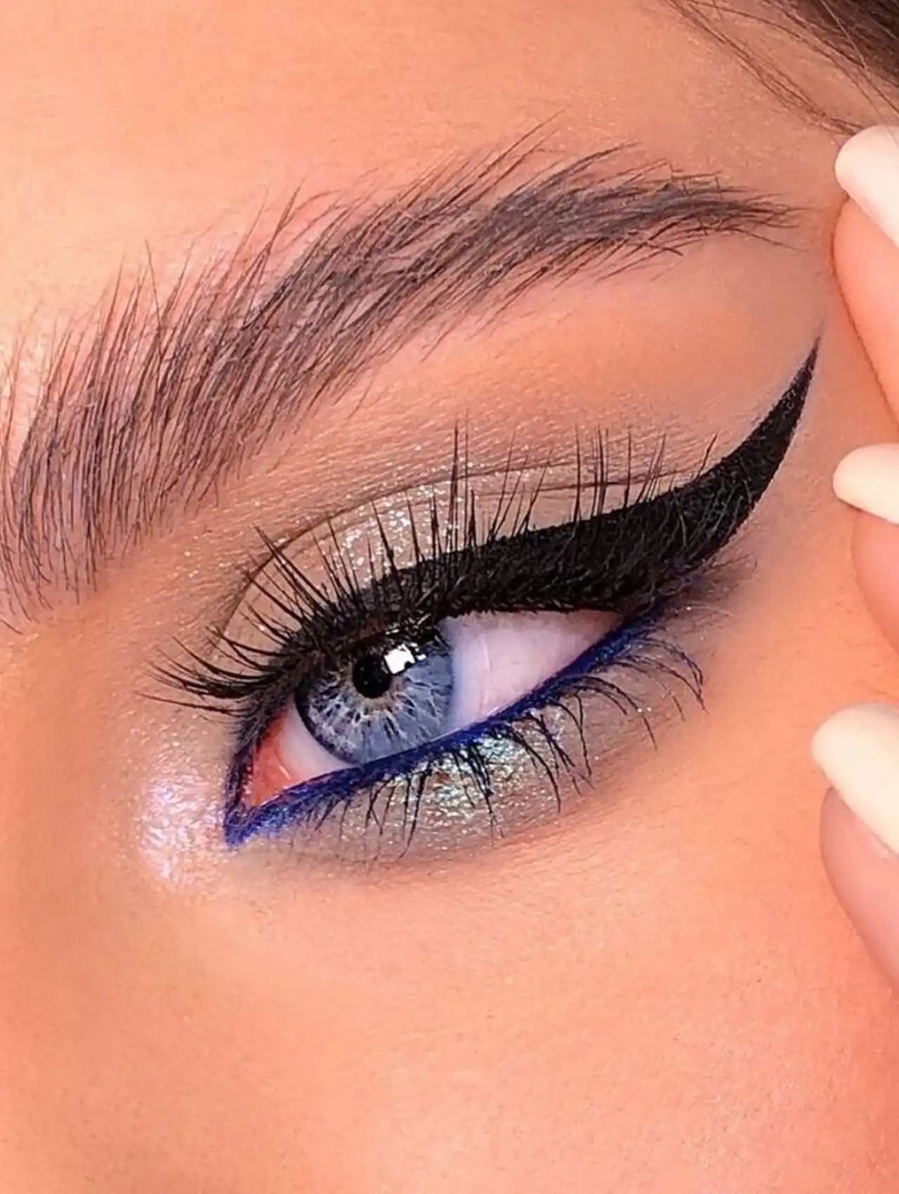 Ojo maquillado con delineador de ojos azul en la línea de agua y pestañas definidas.