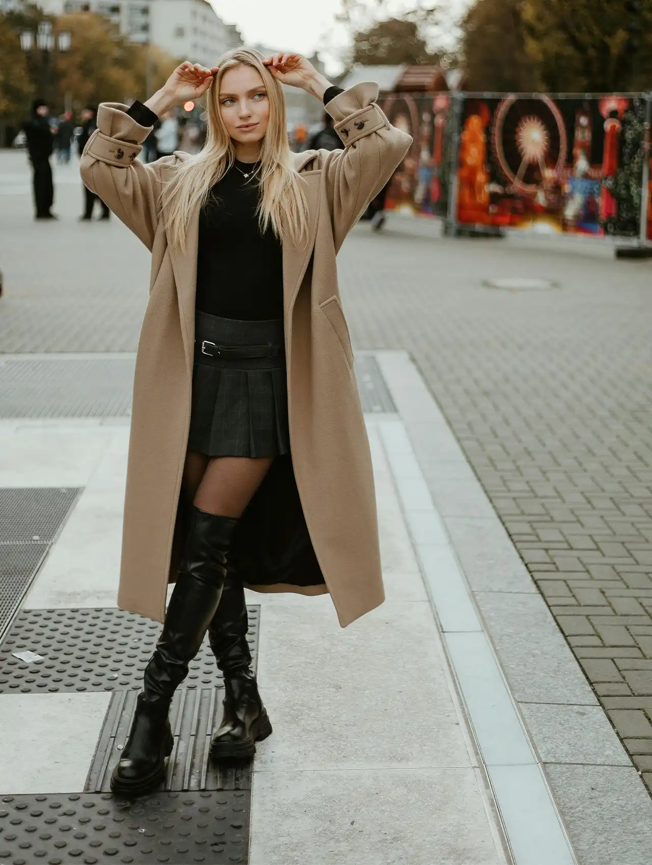 Woman in black best over-the-knee boots paired with beige coat, city street style.