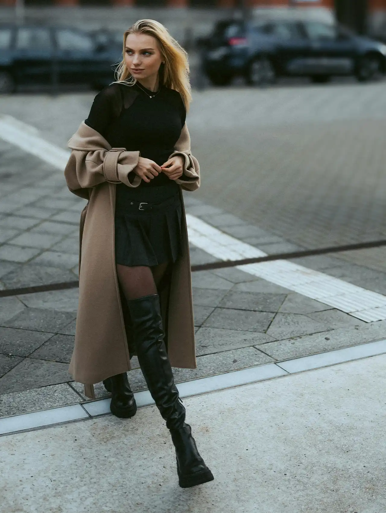 Street style outfit with woman in black best over-the-knee boots and long beige coat.