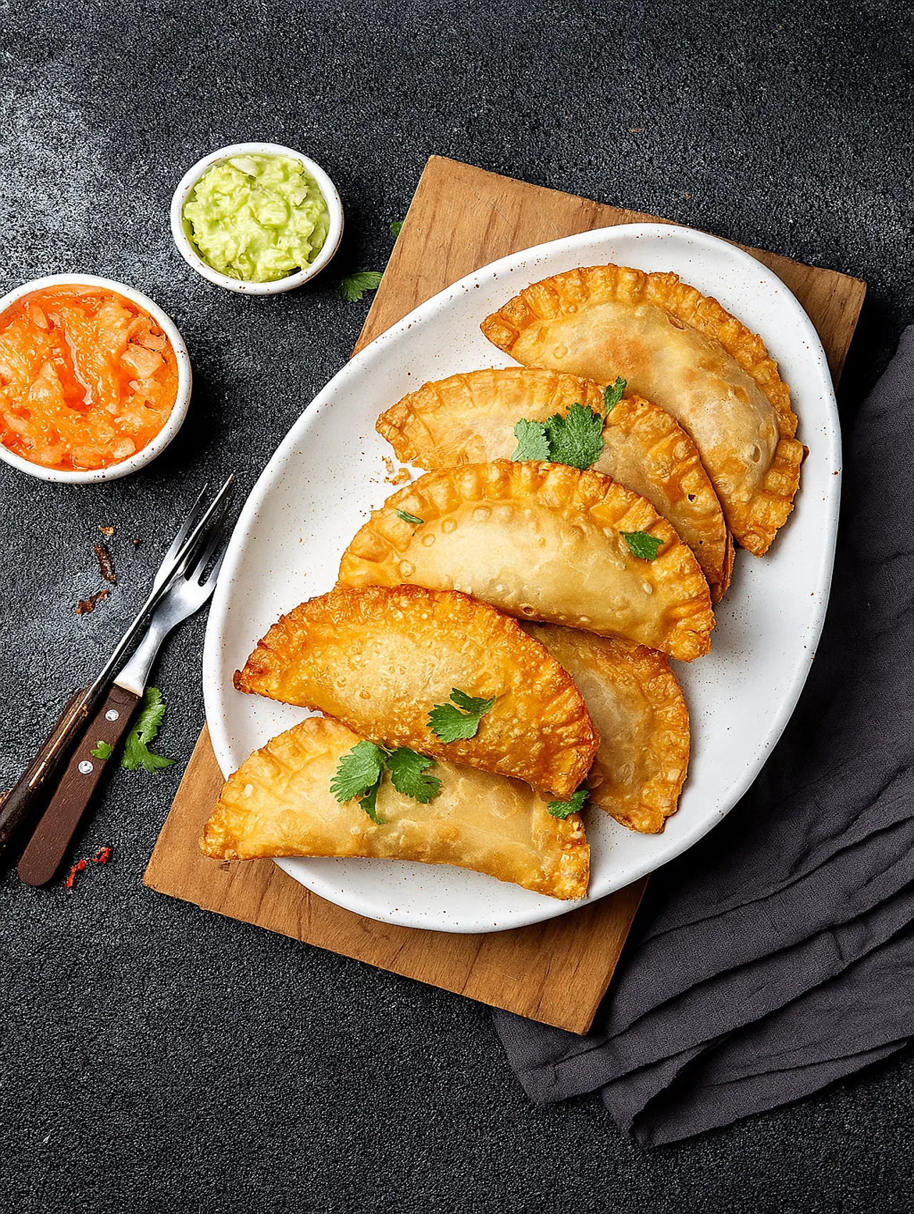 Empanadas de pollo doradas servidas con salsa de tomate y guacamole en un plato blanco