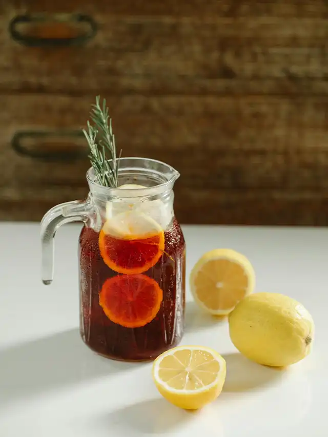 a pitcher of iced tea with orange slices and rosemary