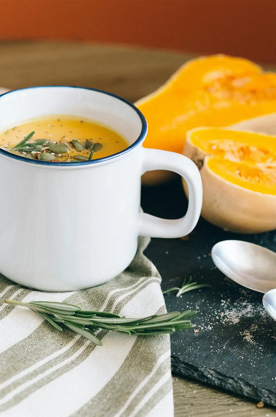 Butternut squash soup in a white mug with fresh rosemary and seeds – fall soup recipes