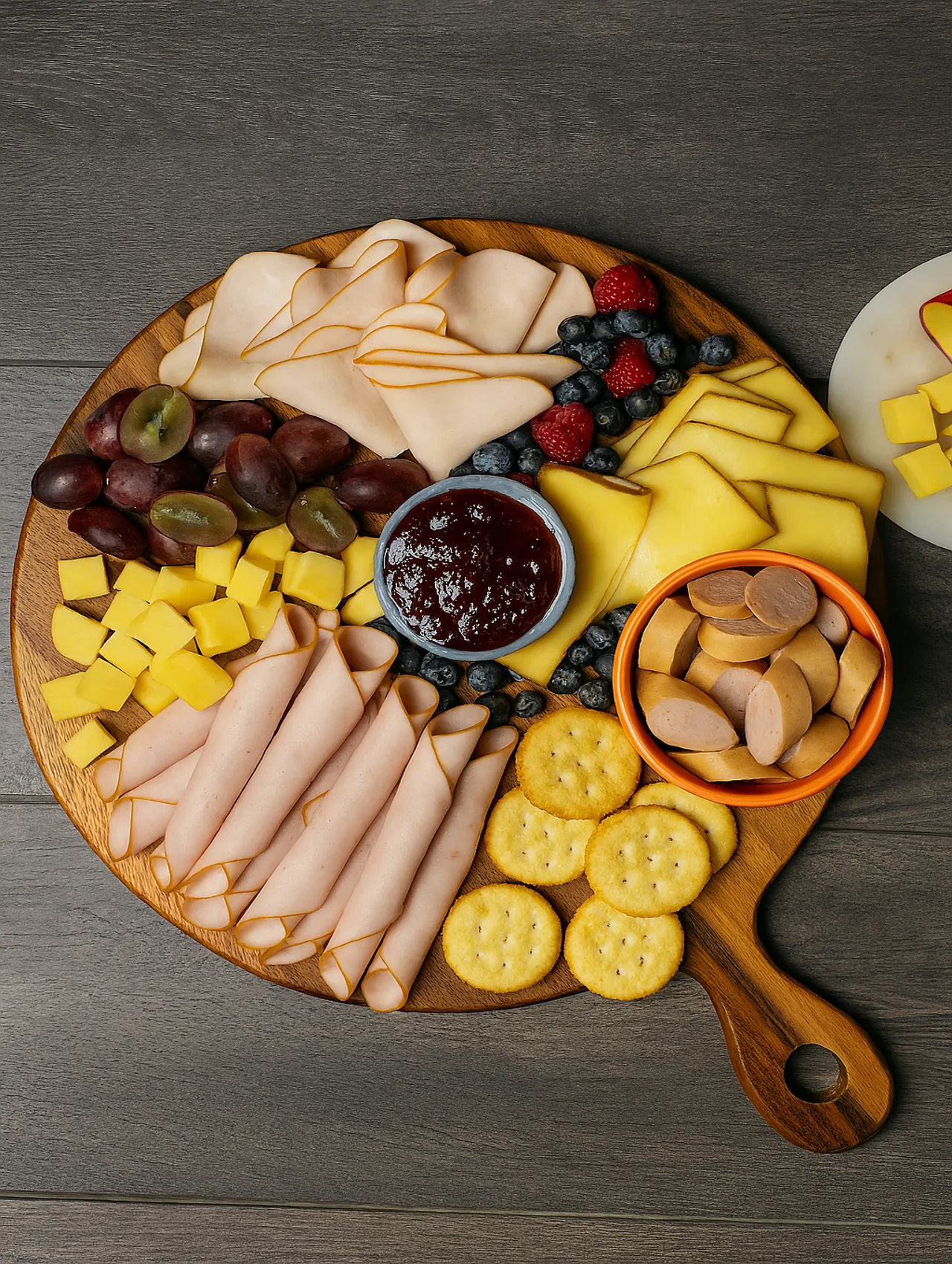 Tabla de lonchas de quesos con frutas frescas, galletas saladas y carnes frías sobre tabla de madera
