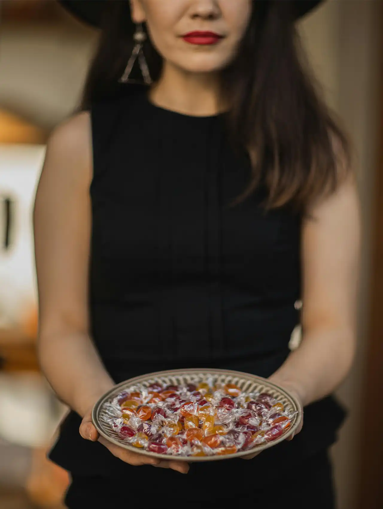 Woman in black holding plate of wrapped candies, vegan halloween candy display.