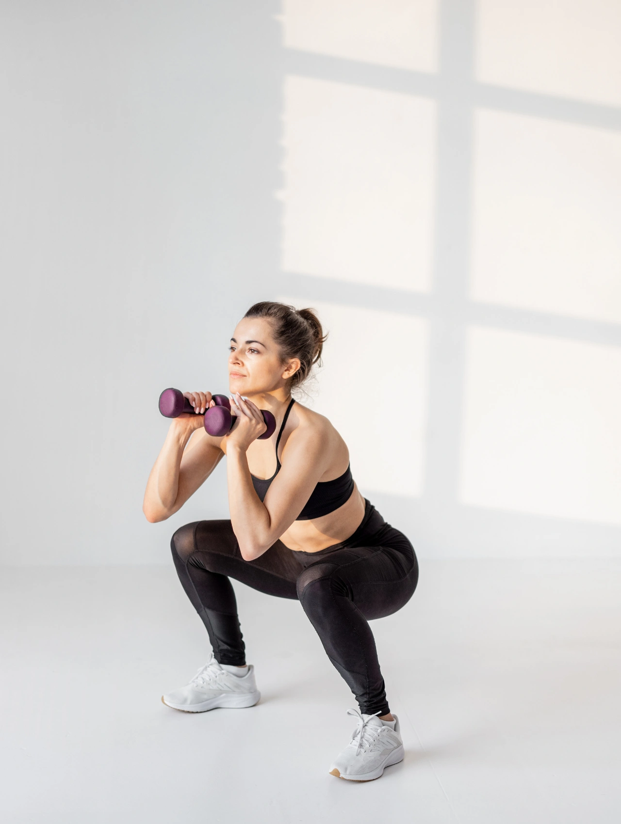 Woman performing a squat with dumbbells indoors, demonstrating a simple move for a Christmas workout for beginners.