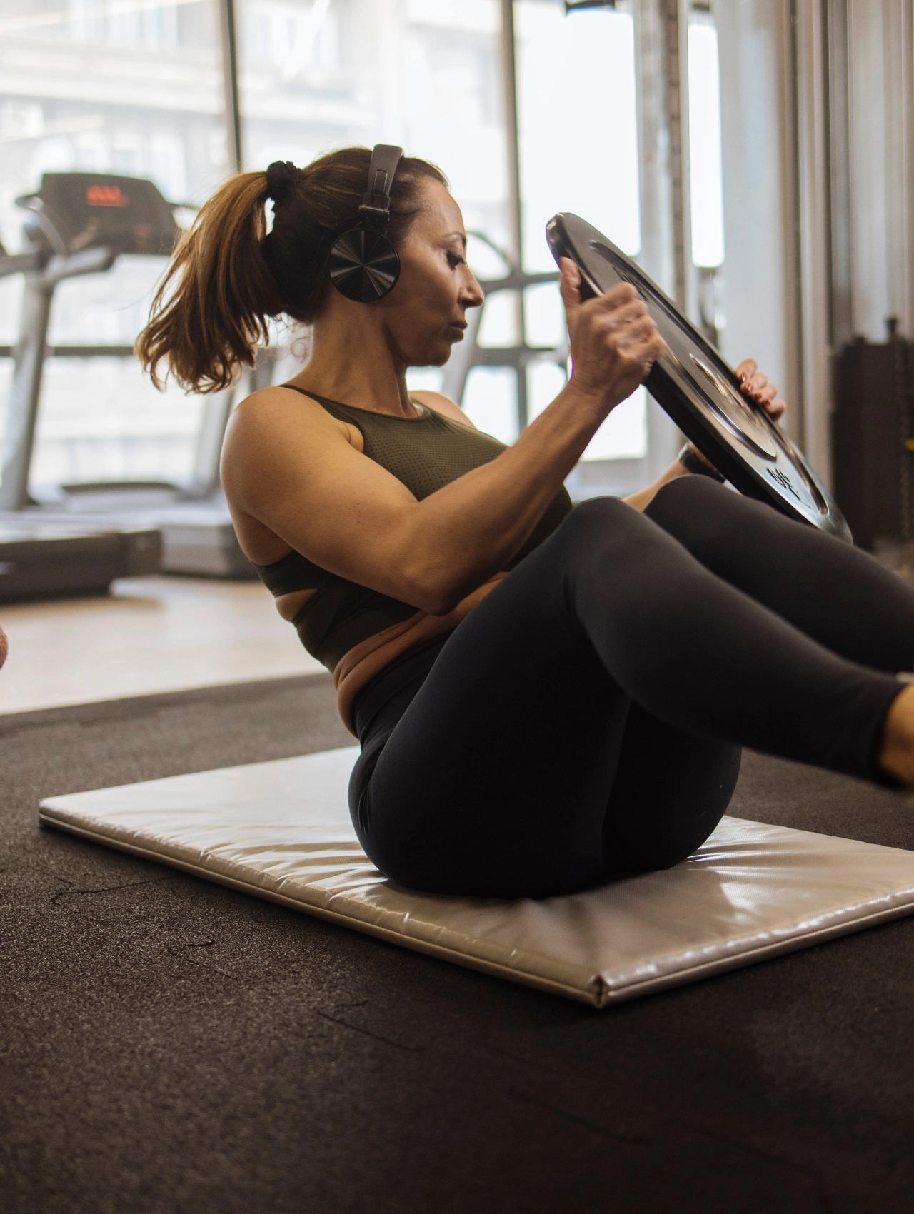 Woman doing core training on a mat in the gym, using a weight plate as part of her Christmas workout.